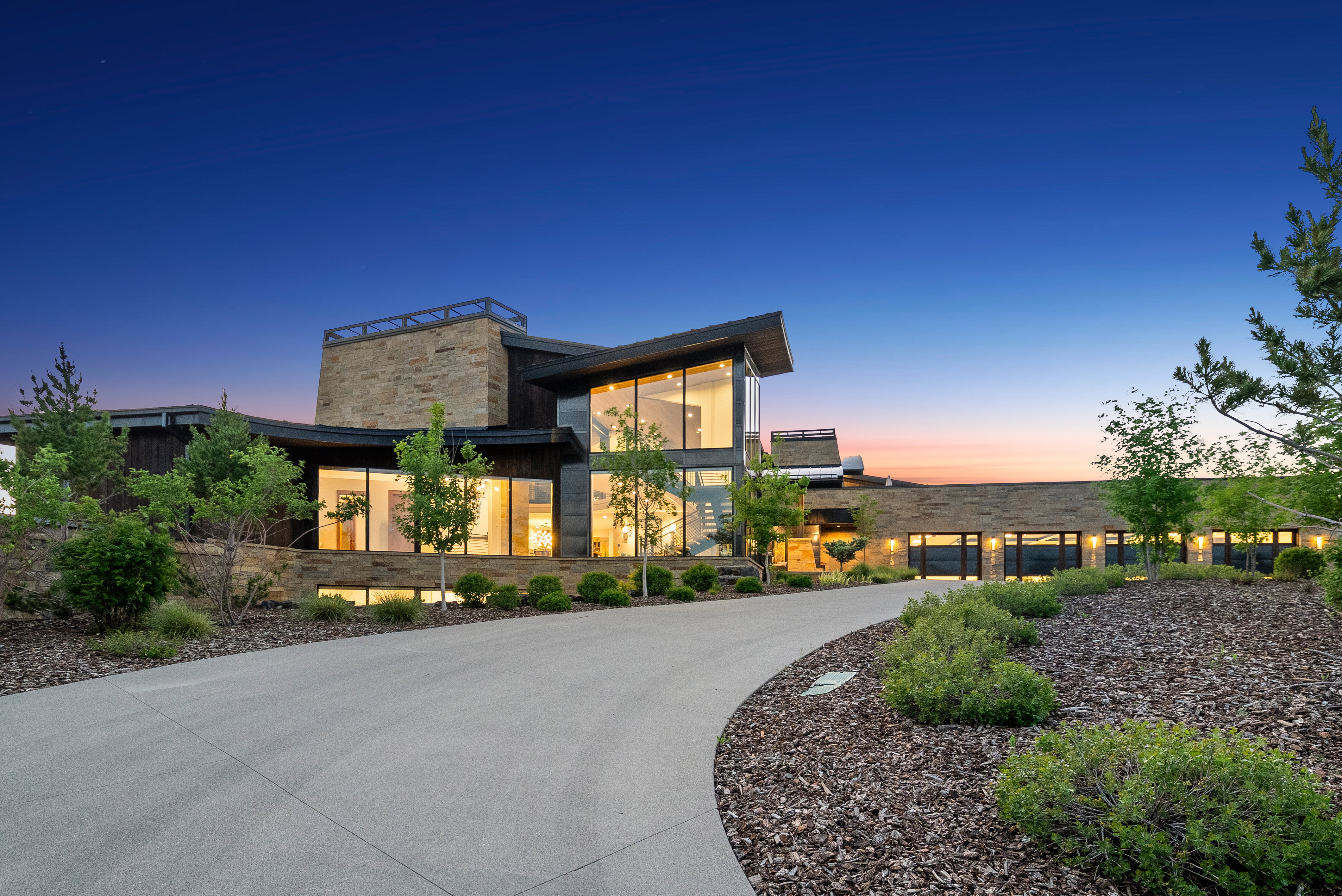 Modern architectural residence featuring stone and wood-clad exterior finishes, extensive window walls, and multiple garage bays