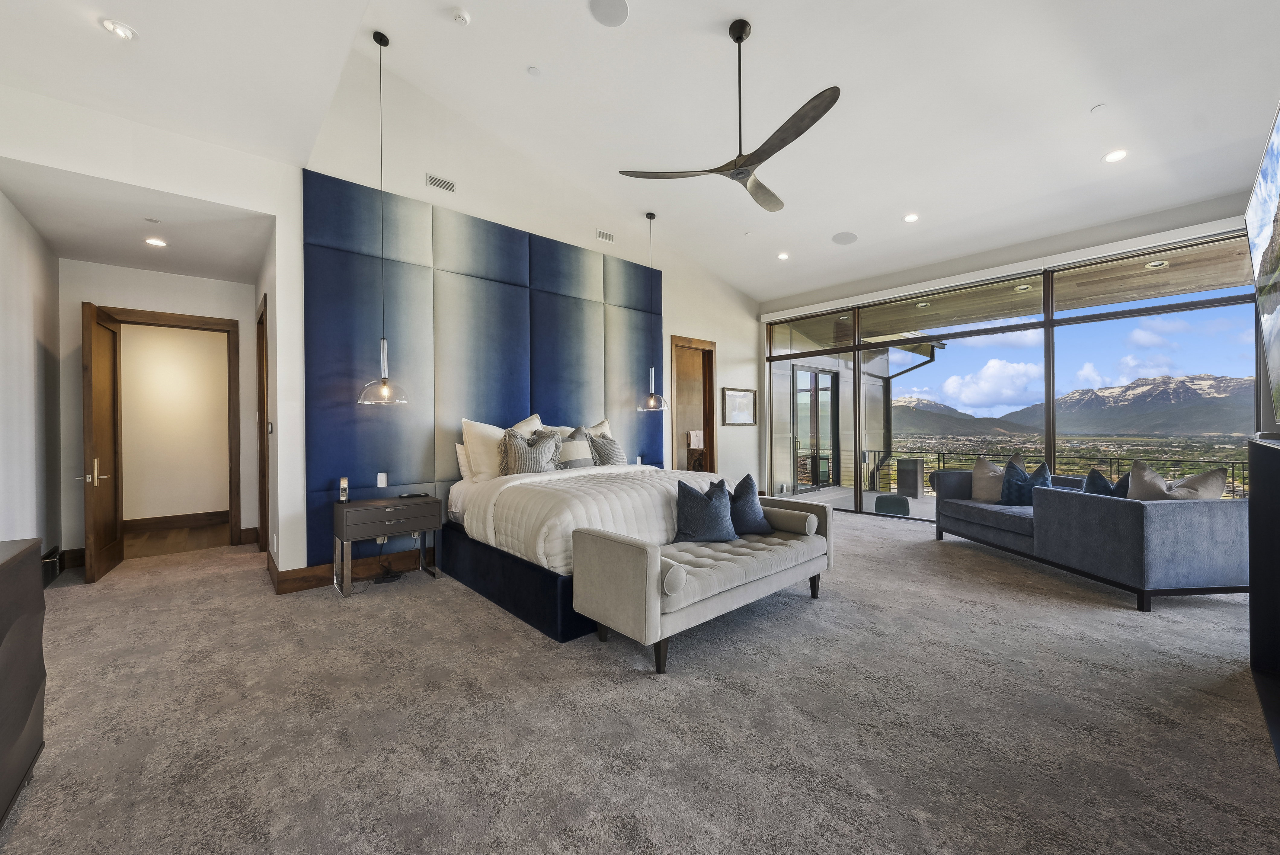 Spacious bedroom featuring large format windows, a contemporary ceiling fan, recessed lighting, and a striking paneled accent wall