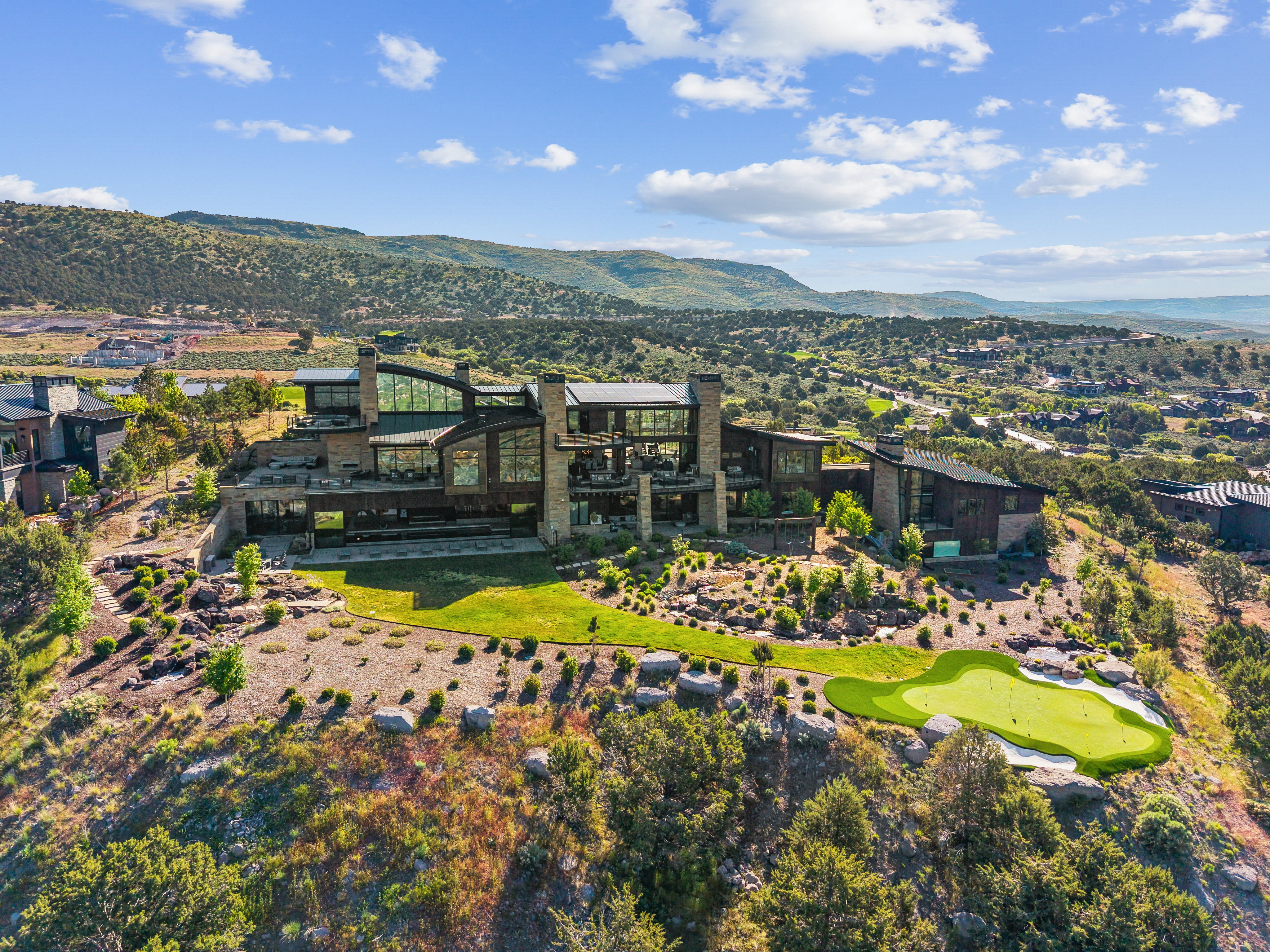 Expansive contemporary residence featuring multiple levels of outdoor living space, a terraced lawn, and a private putting green