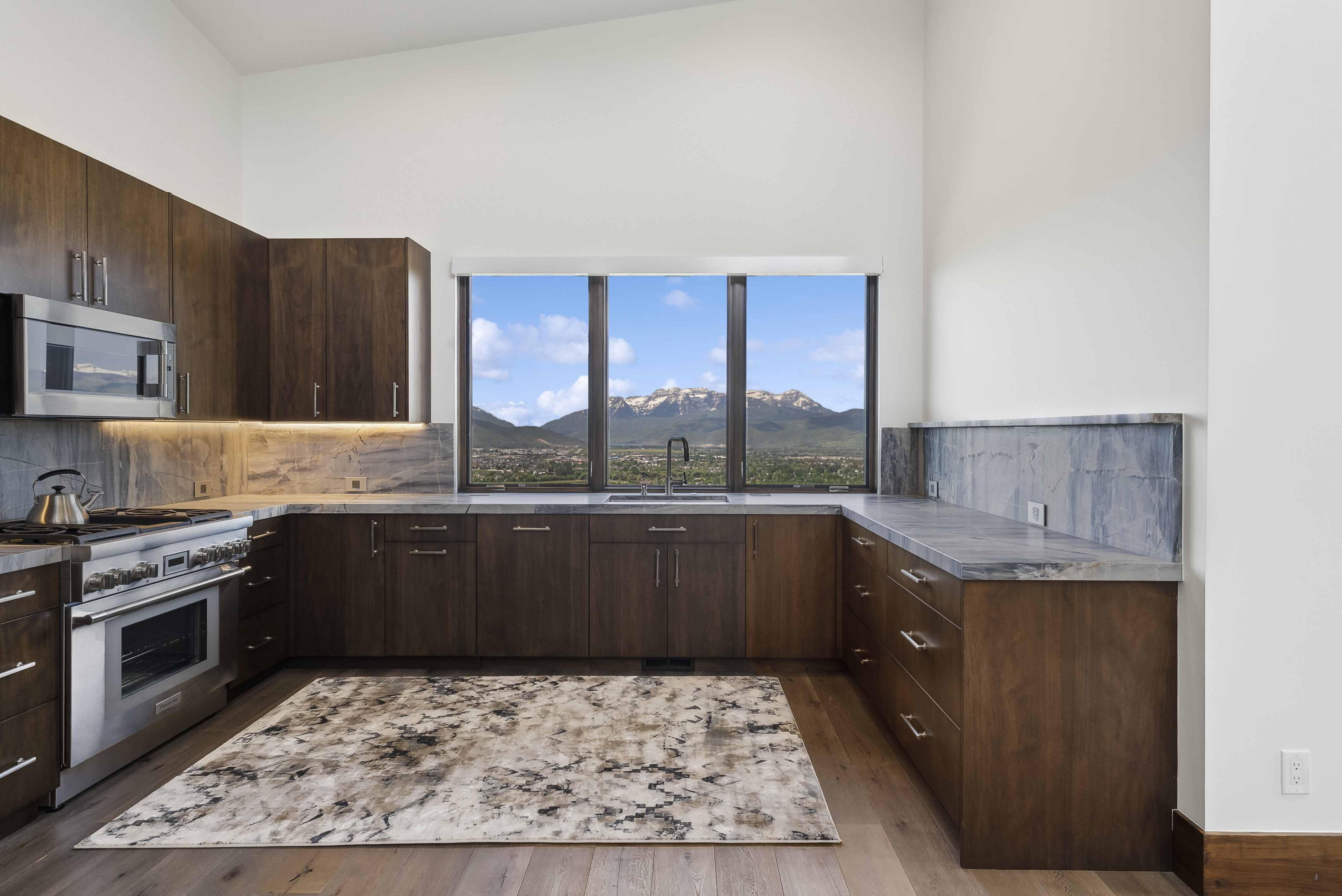 Kitchen featuring wood-finish cabinetry with stainless steel hardware, stone countertops with a matching backsplash, and integrated stainless steel appliances