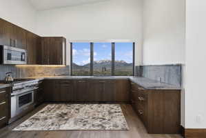 Kitchen featuring wood-finish cabinetry with stainless steel hardware, stone countertops with a matching backsplash, and integrated stainless steel appliances