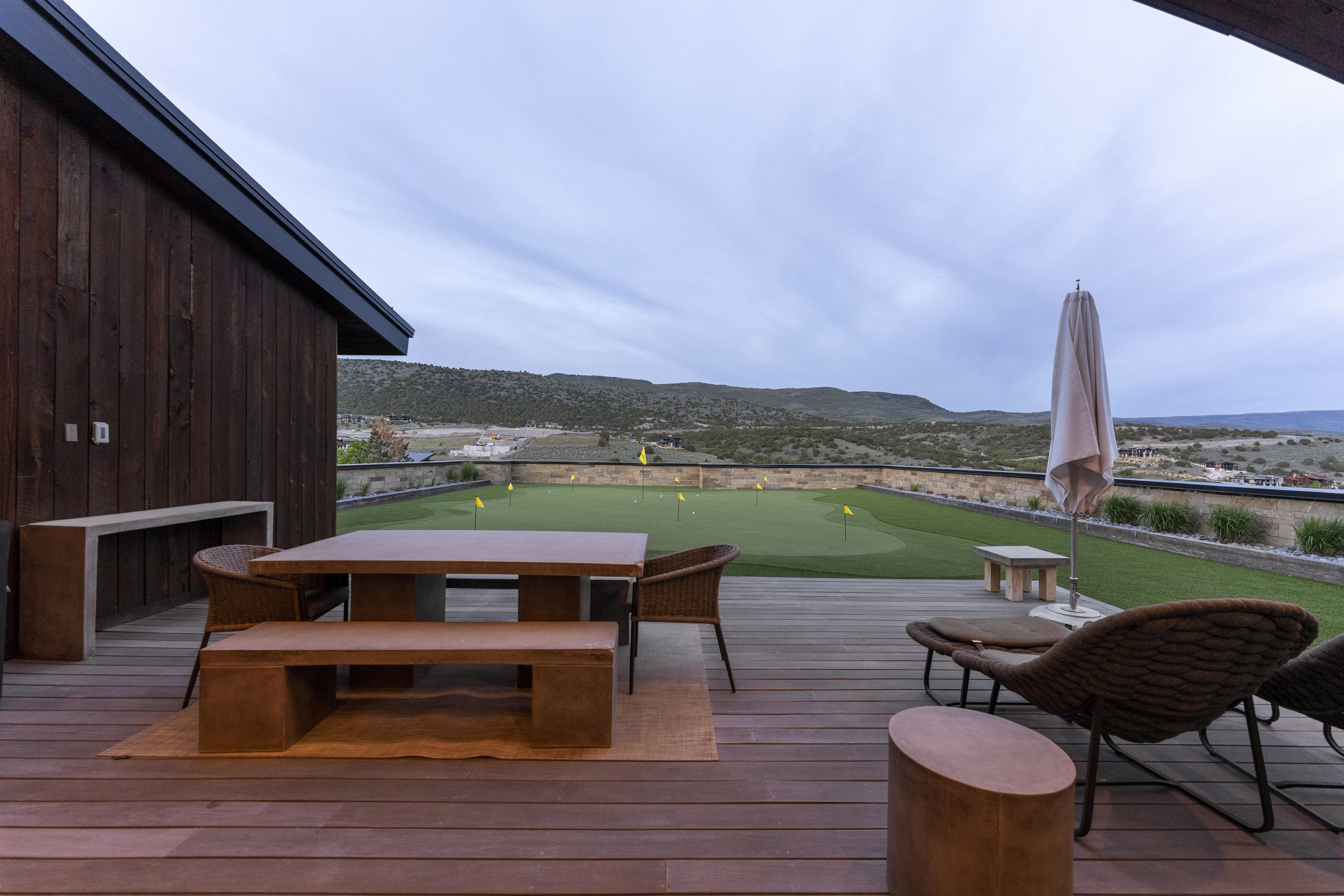 Expansive outdoor deck featuring wood-finish flooring, a built-in putting green with multiple flag positions, and a stone retaining wall