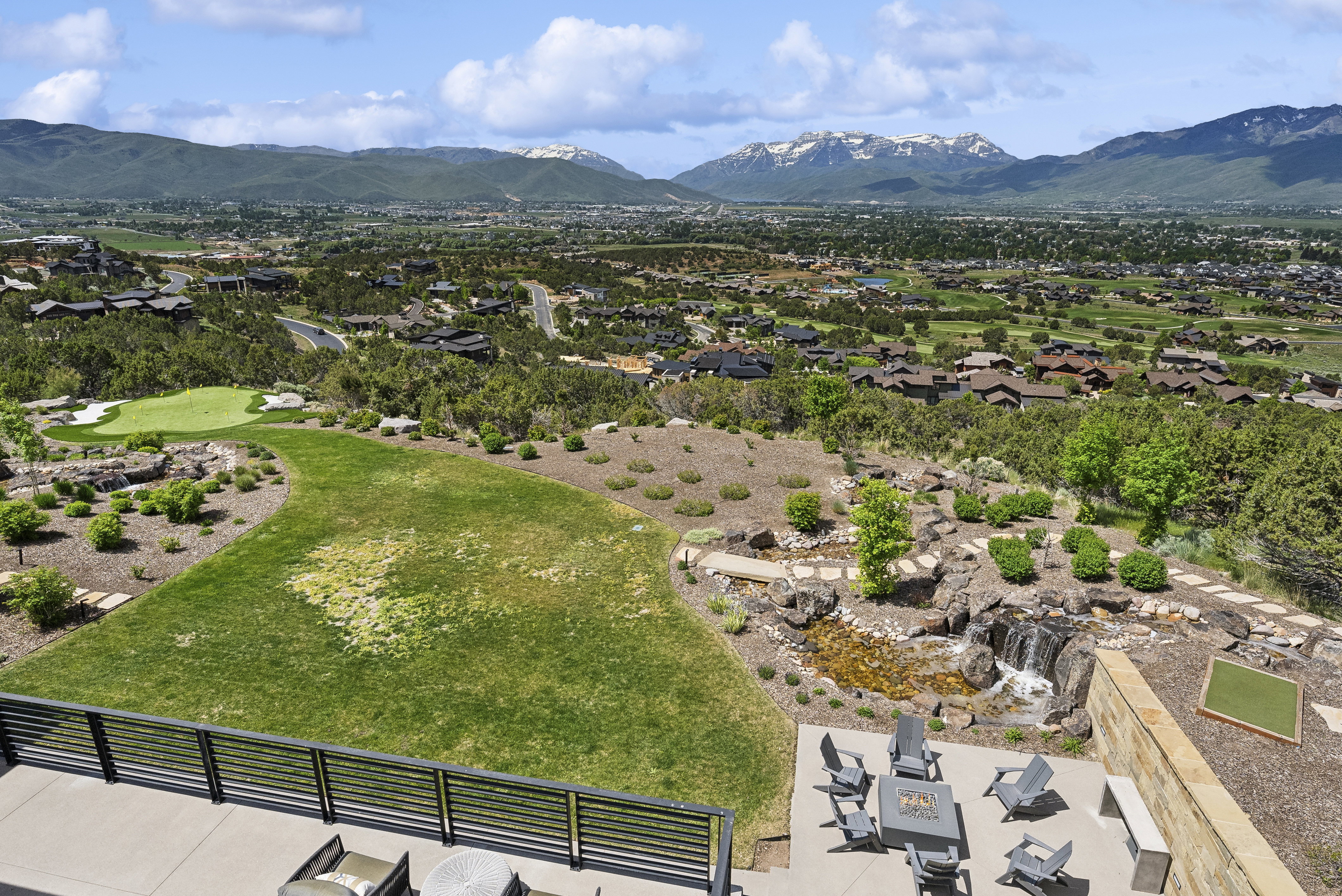 Expansive outdoor living area featuring a stone water feature with a waterfall, a manicured lawn, and a putting green