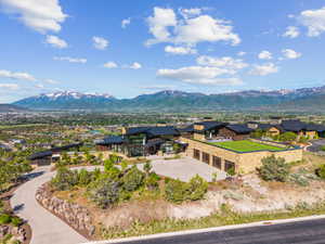Expansive contemporary estate featuring stone and wood facade, a green roof putting area, multiple garages, and a paved driveway with natural rock landscaping