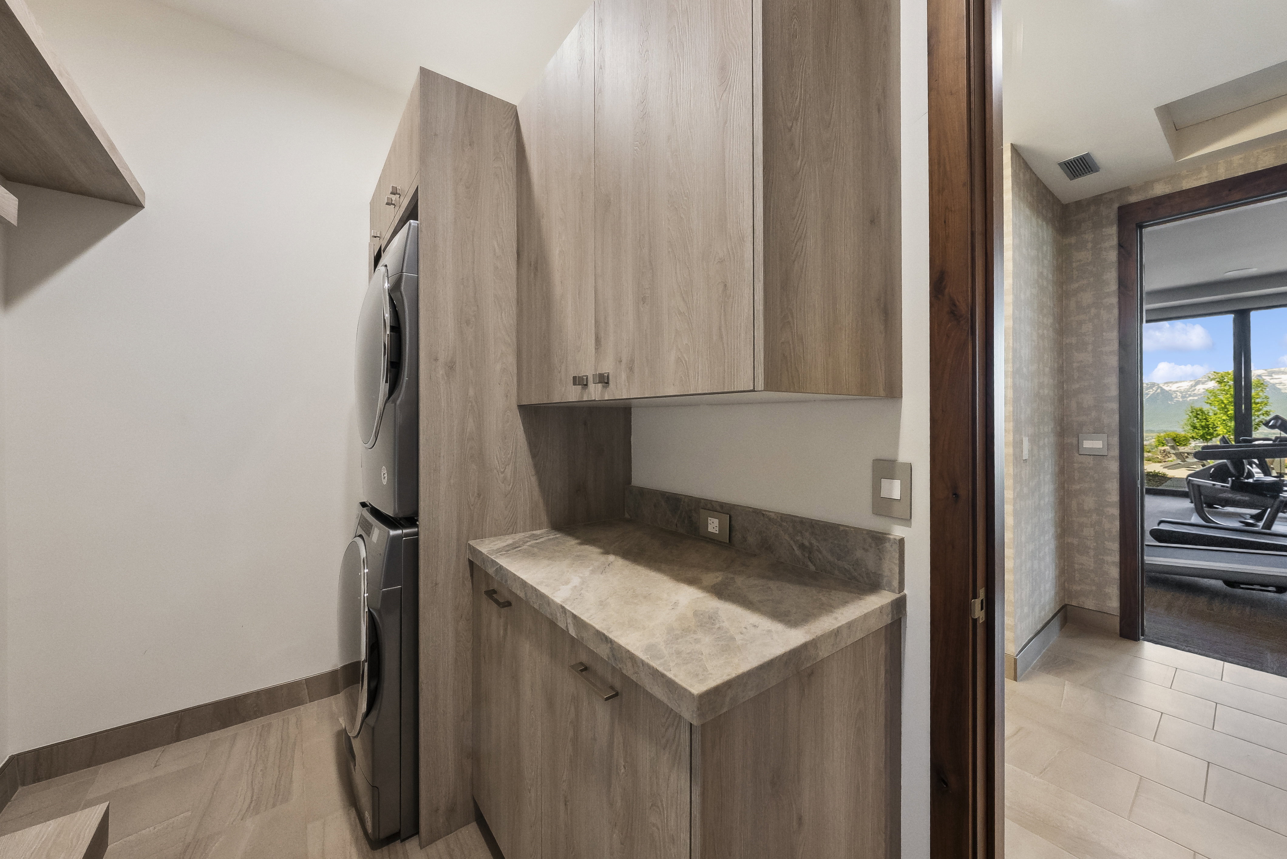 Dedicated laundry area featuring stacked appliances, wood-finish cabinetry, and a stone countertop