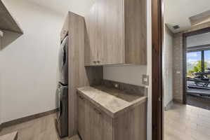 Dedicated laundry area featuring stacked appliances, wood-finish cabinetry, and a stone countertop