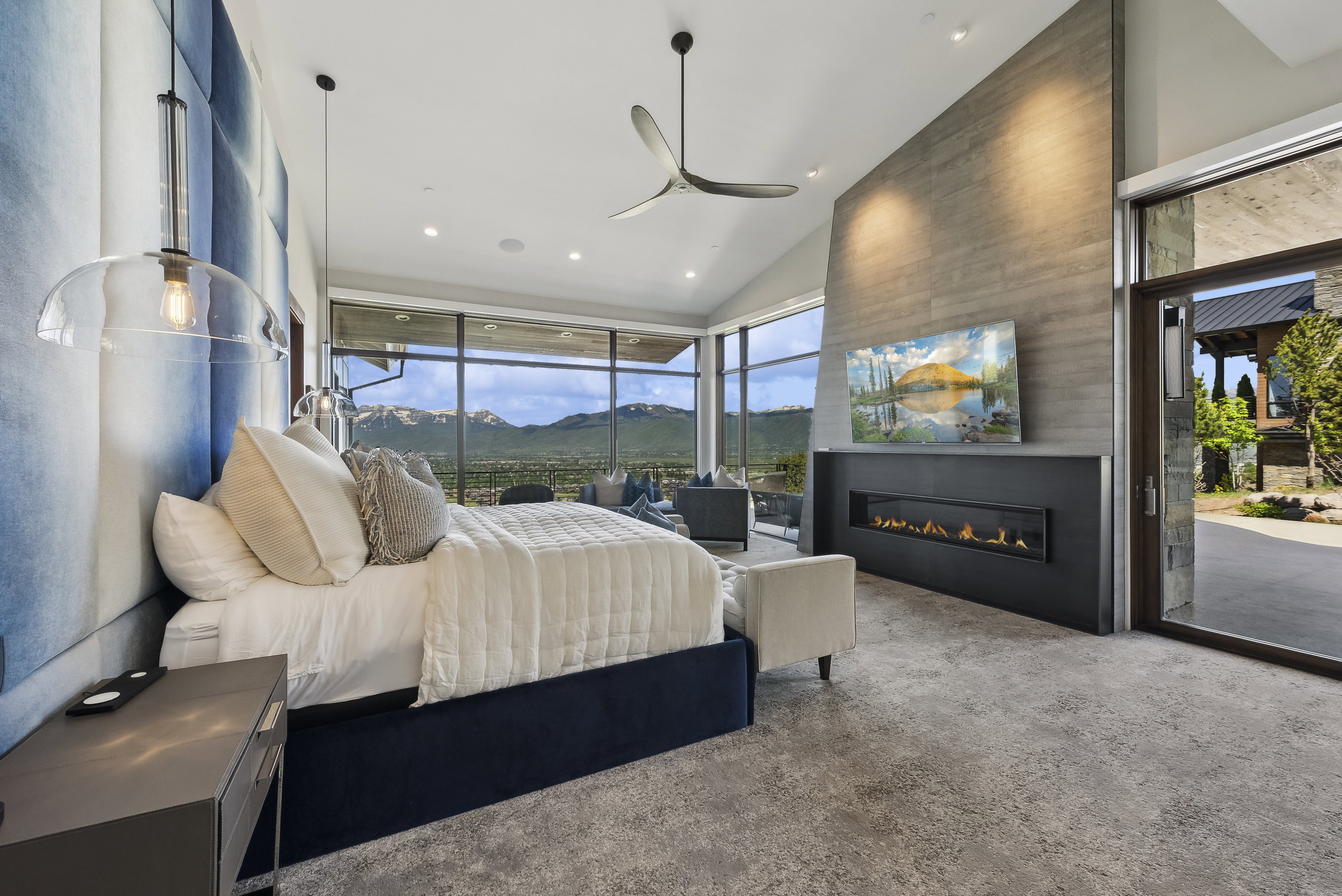 Spacious bedroom featuring floor-to-ceiling windows, a linear gas fireplace, a large concrete-finish accent wall, and a full-light entry door