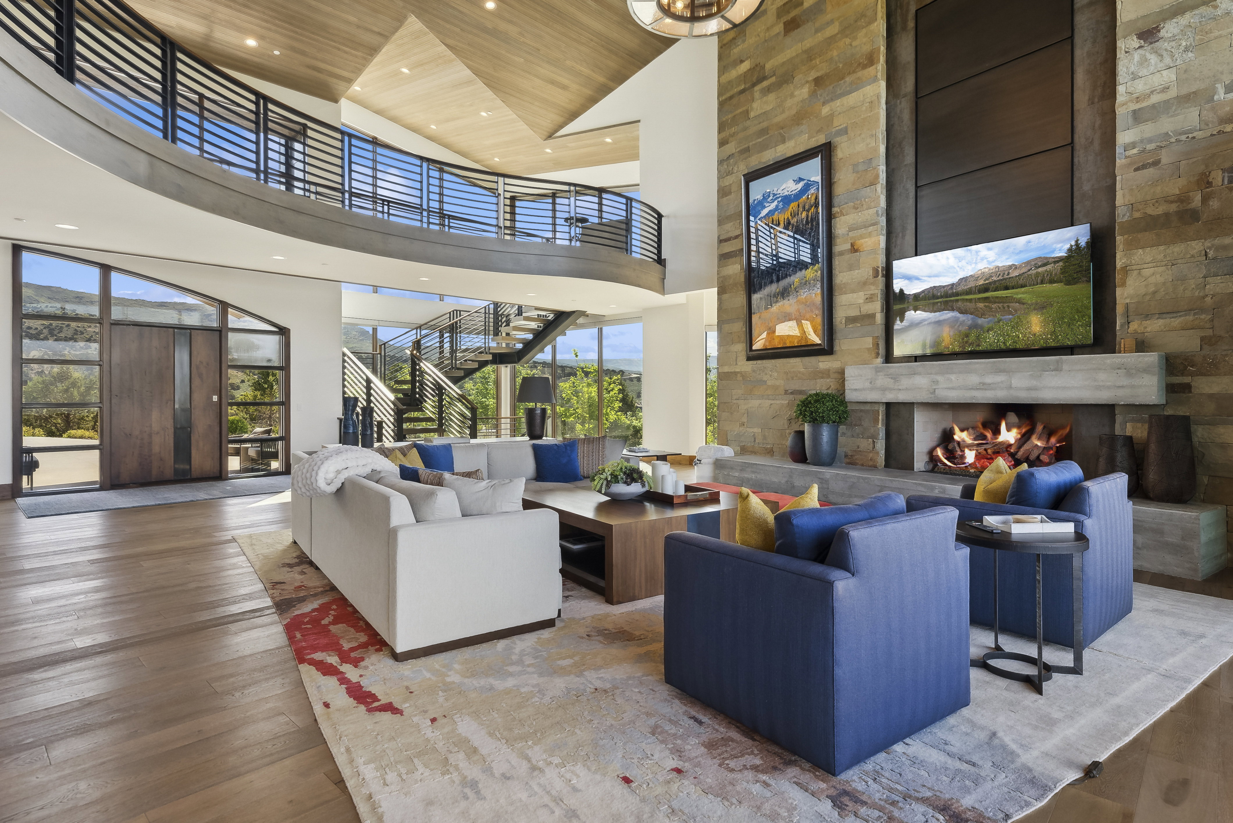 Spacious living area featuring a floor-to-ceiling stone fireplace with a substantial hearth, wood-finish flooring, and a two-story ceiling with wood paneling