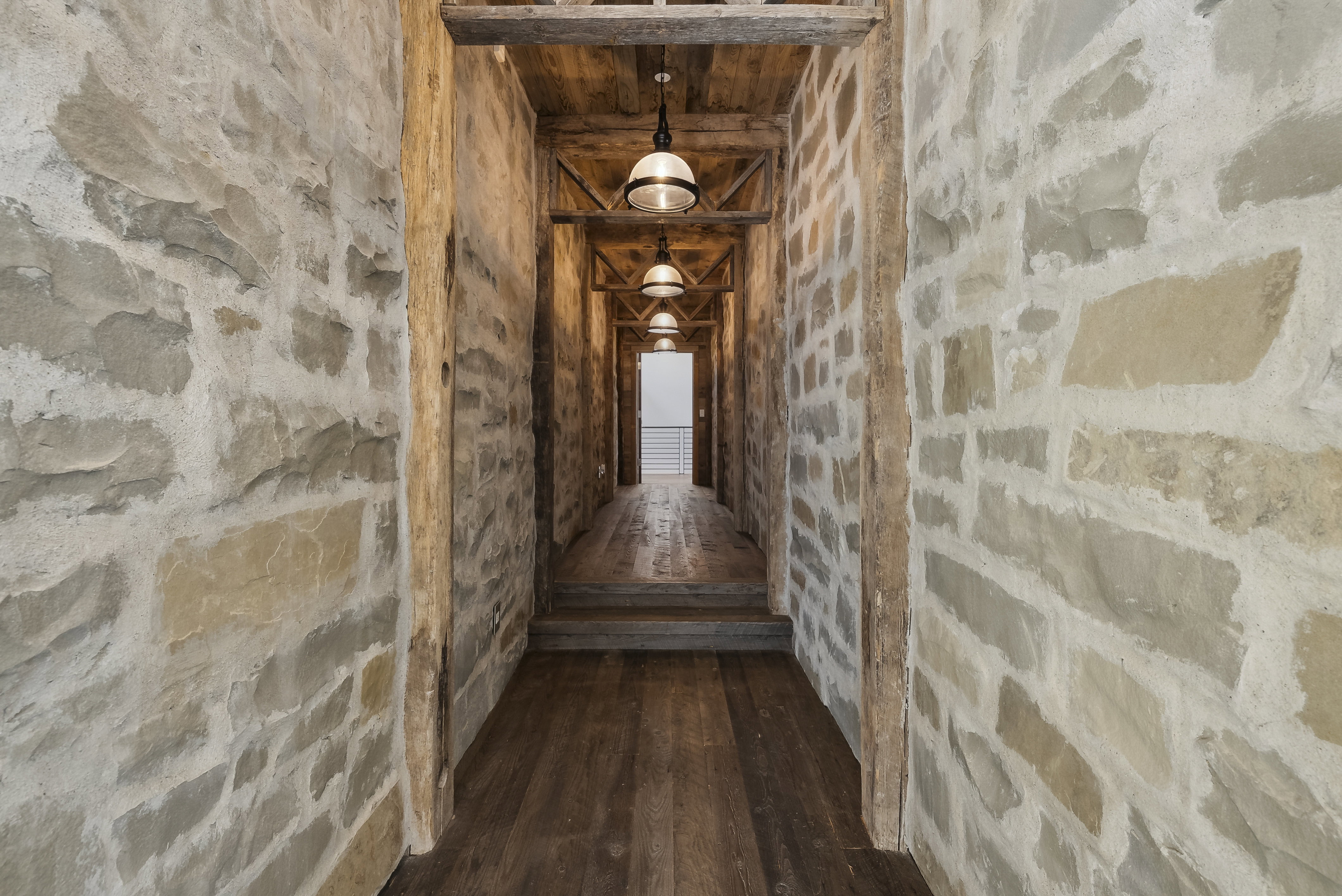 Stone-clad hallway featuring wood-finish flooring and exposed timber ceiling beams