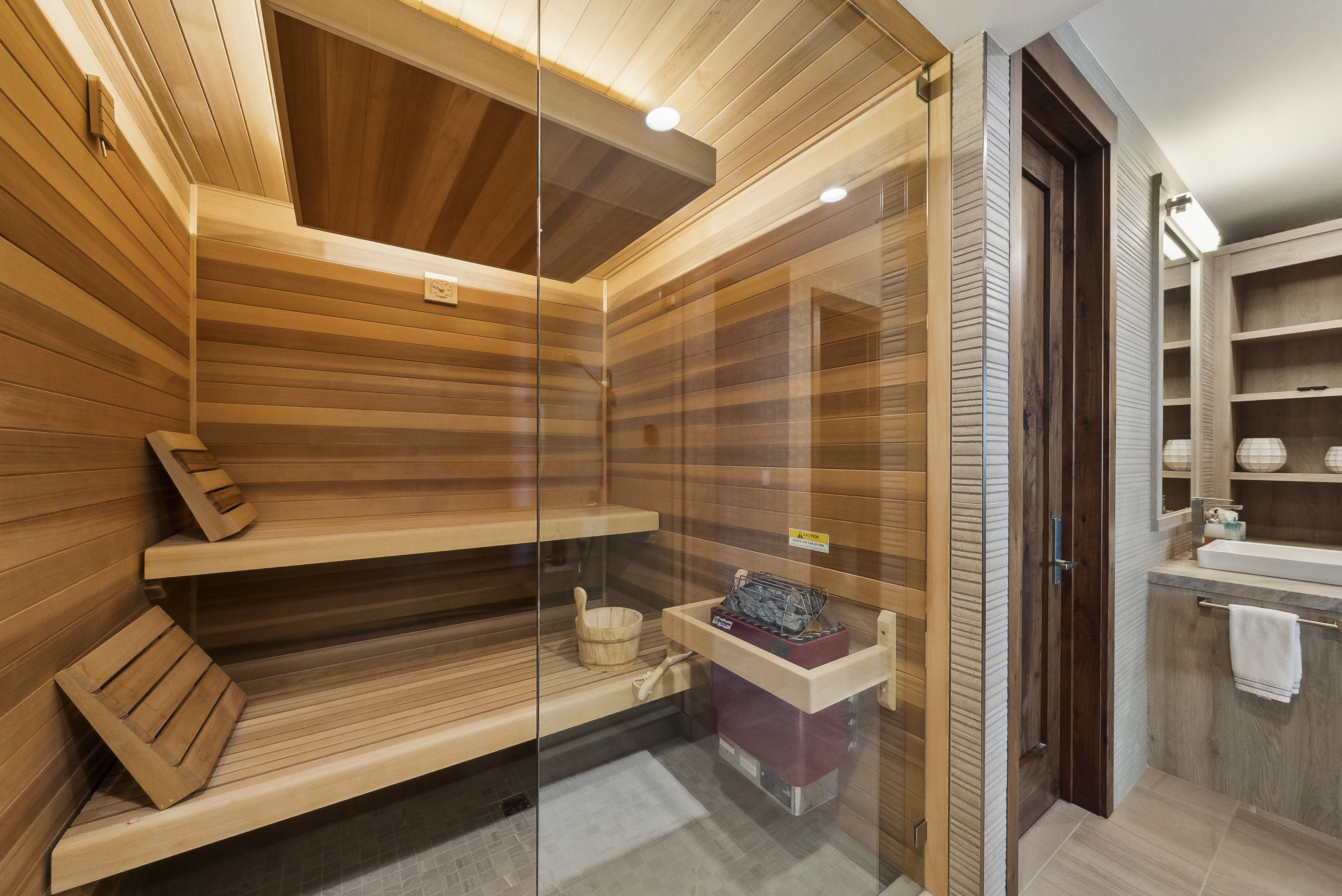 Private sauna featuring wood-paneled walls and ceiling, multi-level benches, a glass enclosure, and an electric sauna heater