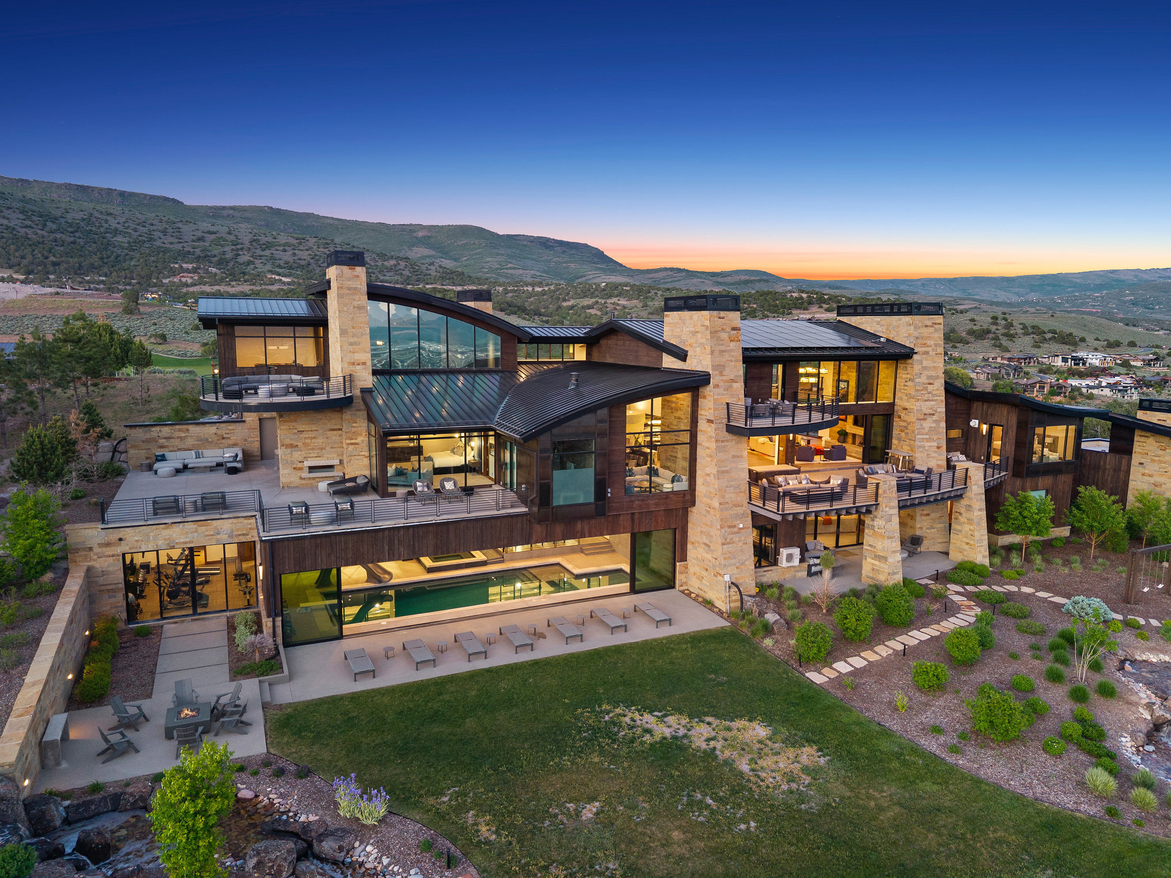 Contemporary multi-level residence featuring expansive windows, natural stone and wood-finish siding, multiple outdoor patios, and an indoor swimming pool