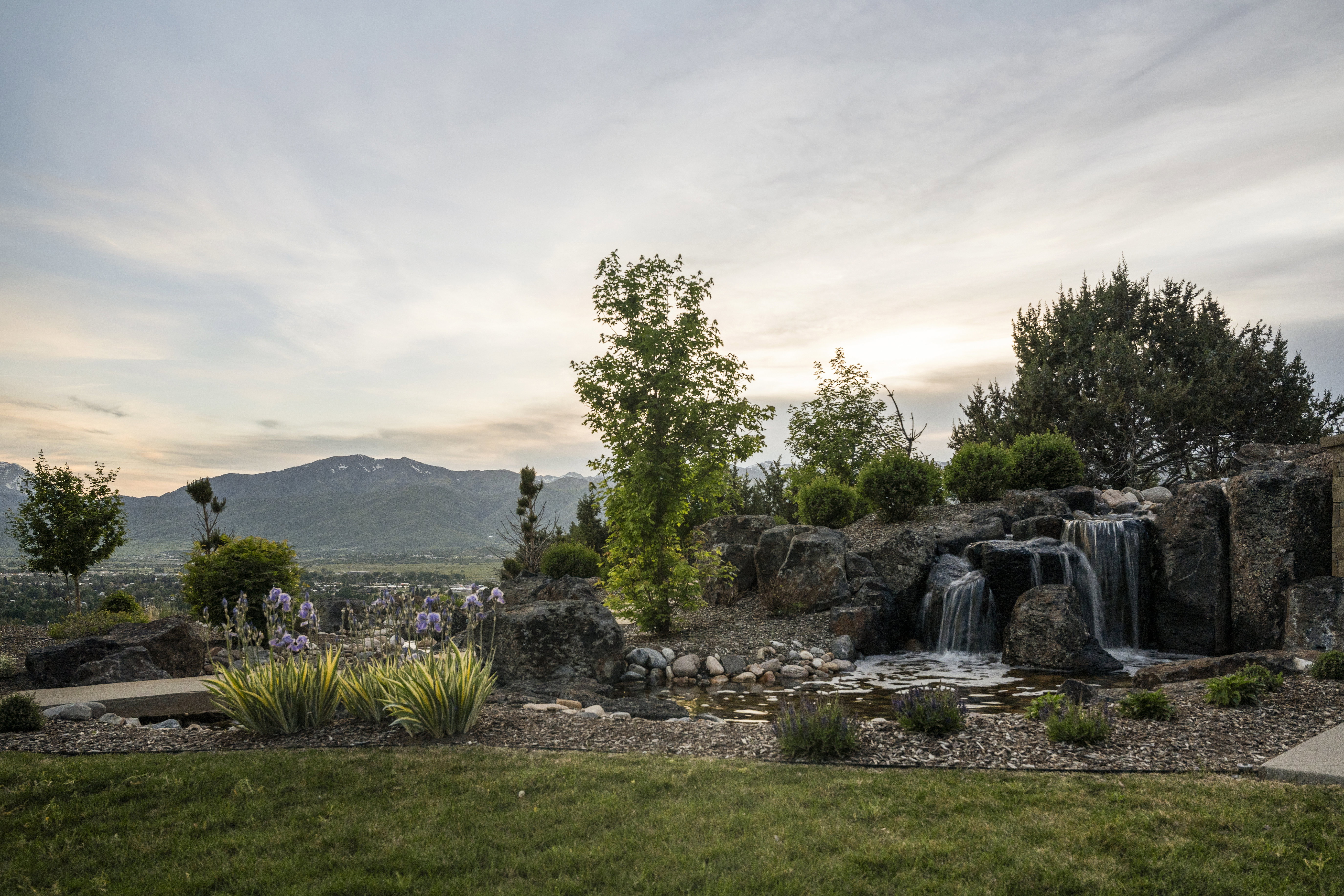 Expansive hardscaping featuring a multi-tiered rock waterfall with a pond, surrounded by lush landscaping