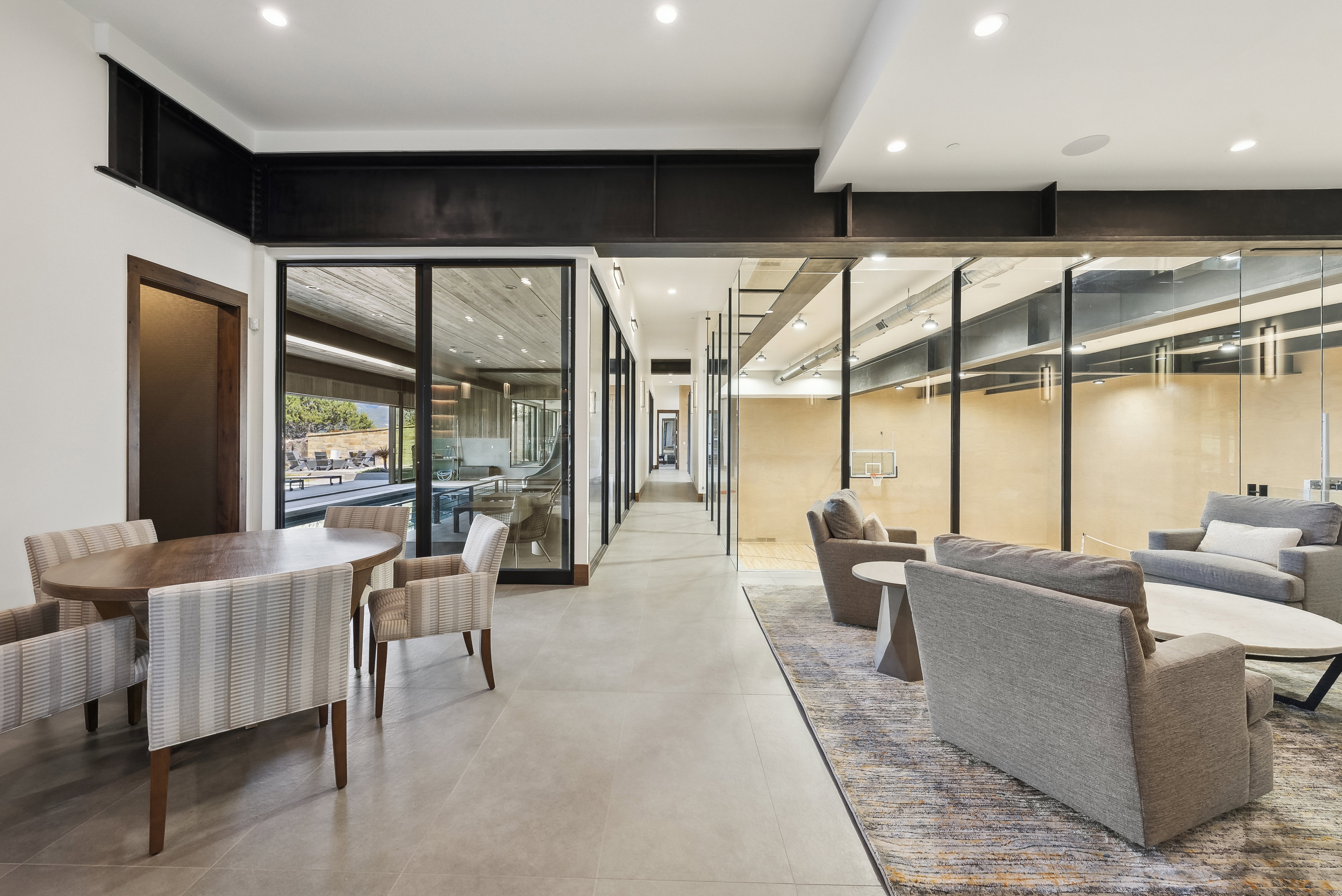 Spacious interior hallway featuring large-format tile flooring, exposed structural beams, recessed lighting, and a glass partition wall