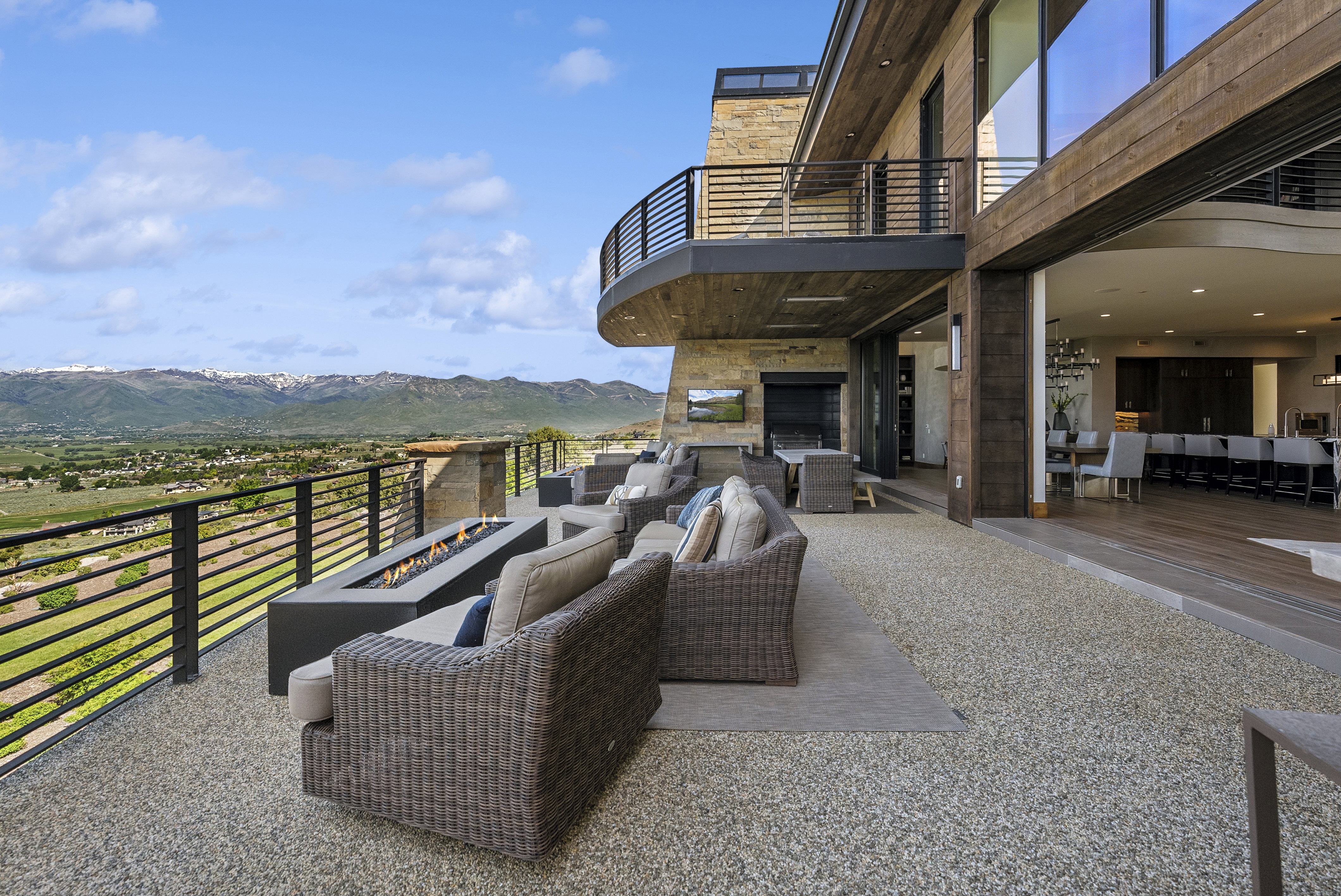 Expansive outdoor patio with a linear fire pit, pebble-aggregate flooring, and modern horizontal railings