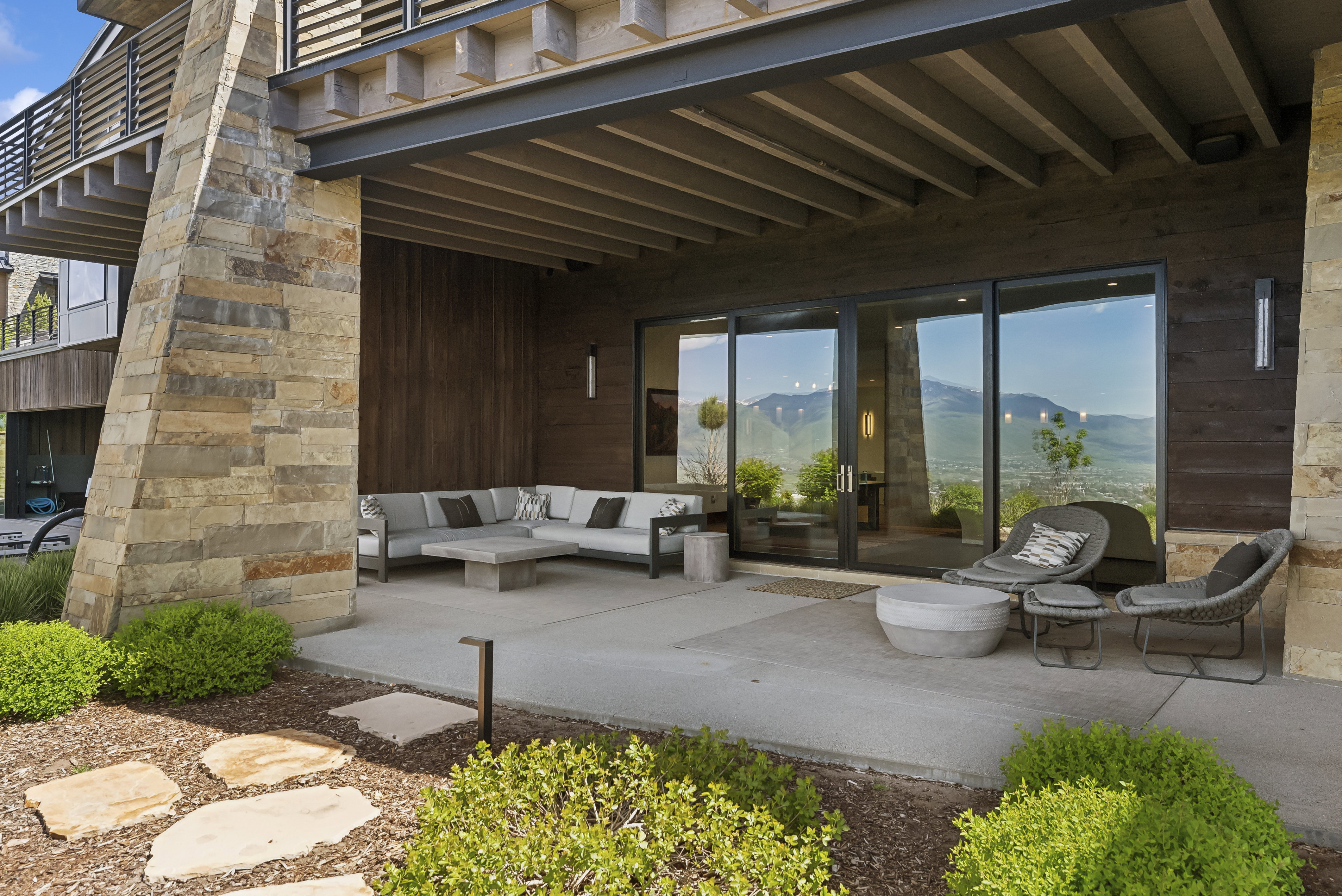 Expansive concrete patio featuring a stacked stone support column, dark wood-finish exterior siding, and large sliding glass doors