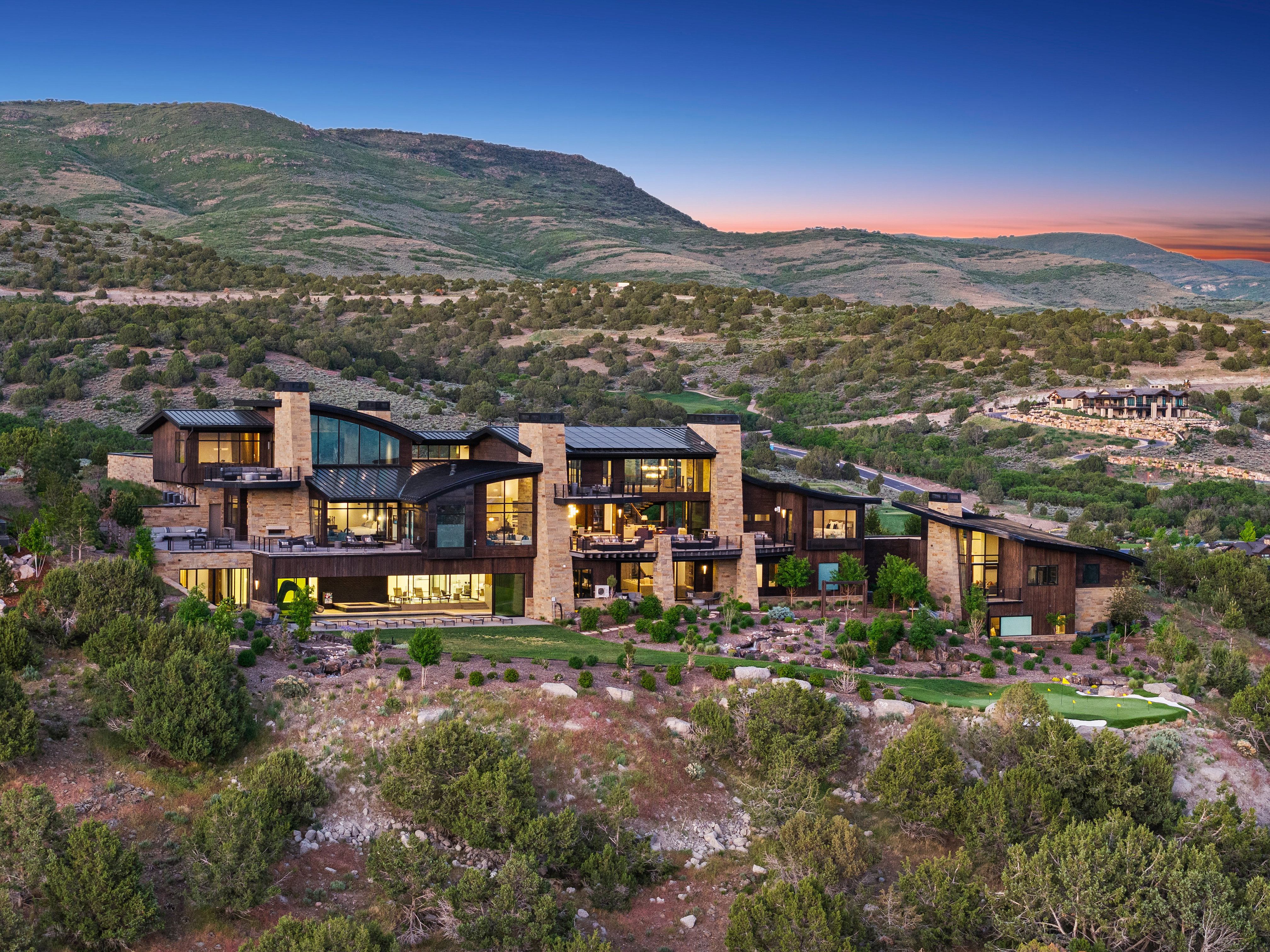Expansive contemporary residence featuring multiple levels, stone and wood-finish exterior accents, extensive window walls, multiple balconies, and a putting green