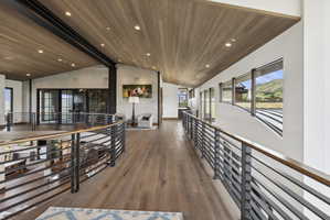 Second-story hallway featuring wood-finish flooring, a slatted wood ceiling with recessed lighting, and modern metal railings with wood top rails