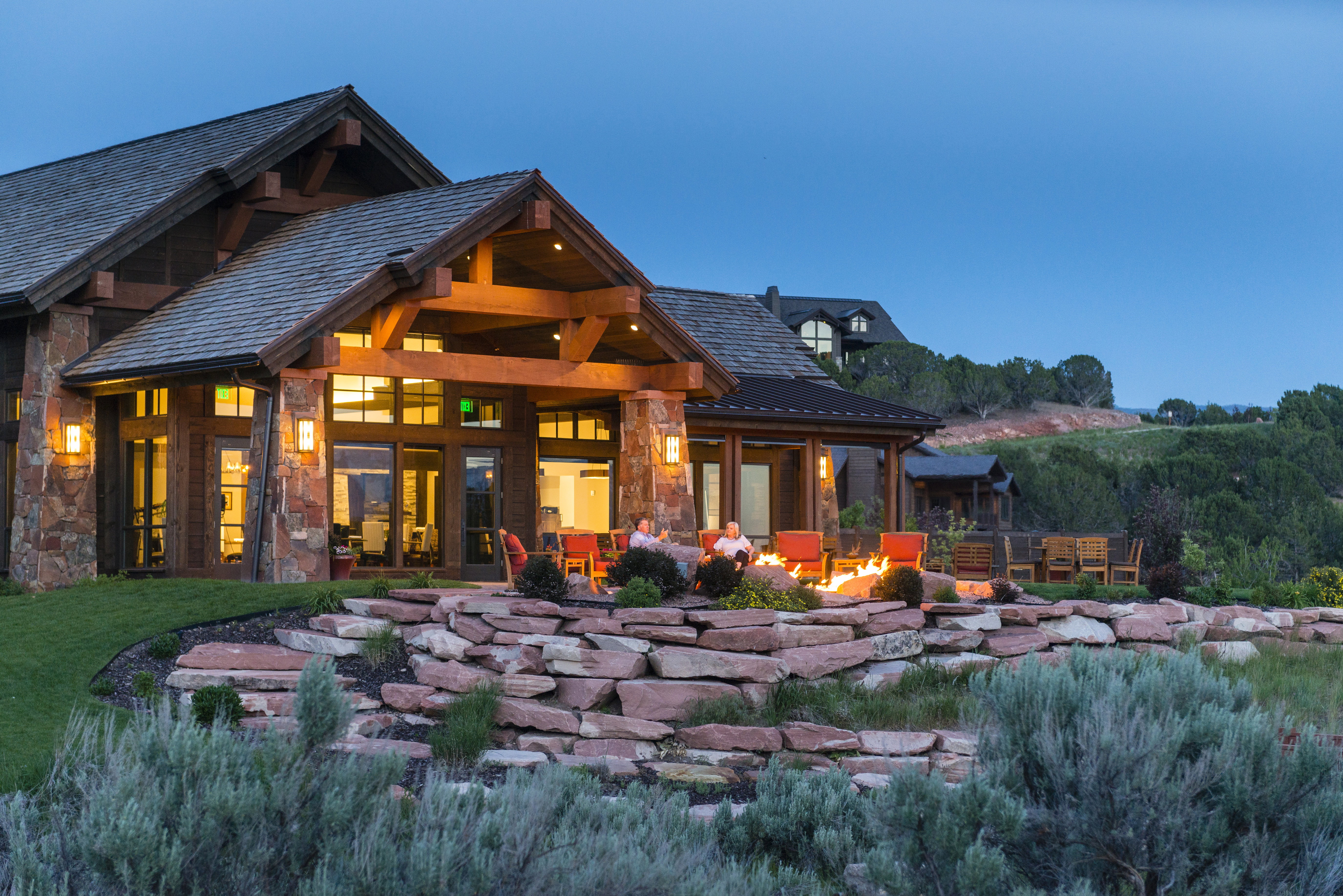 Stone and timber-frame exterior featuring multiple gables, a covered patio with a built-in fire pit, expansive glass doors, and integrated outdoor lighting