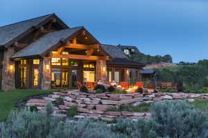 Stone and timber-frame exterior featuring multiple gables, a covered patio with a built-in fire pit, expansive glass doors, and integrated outdoor lighting