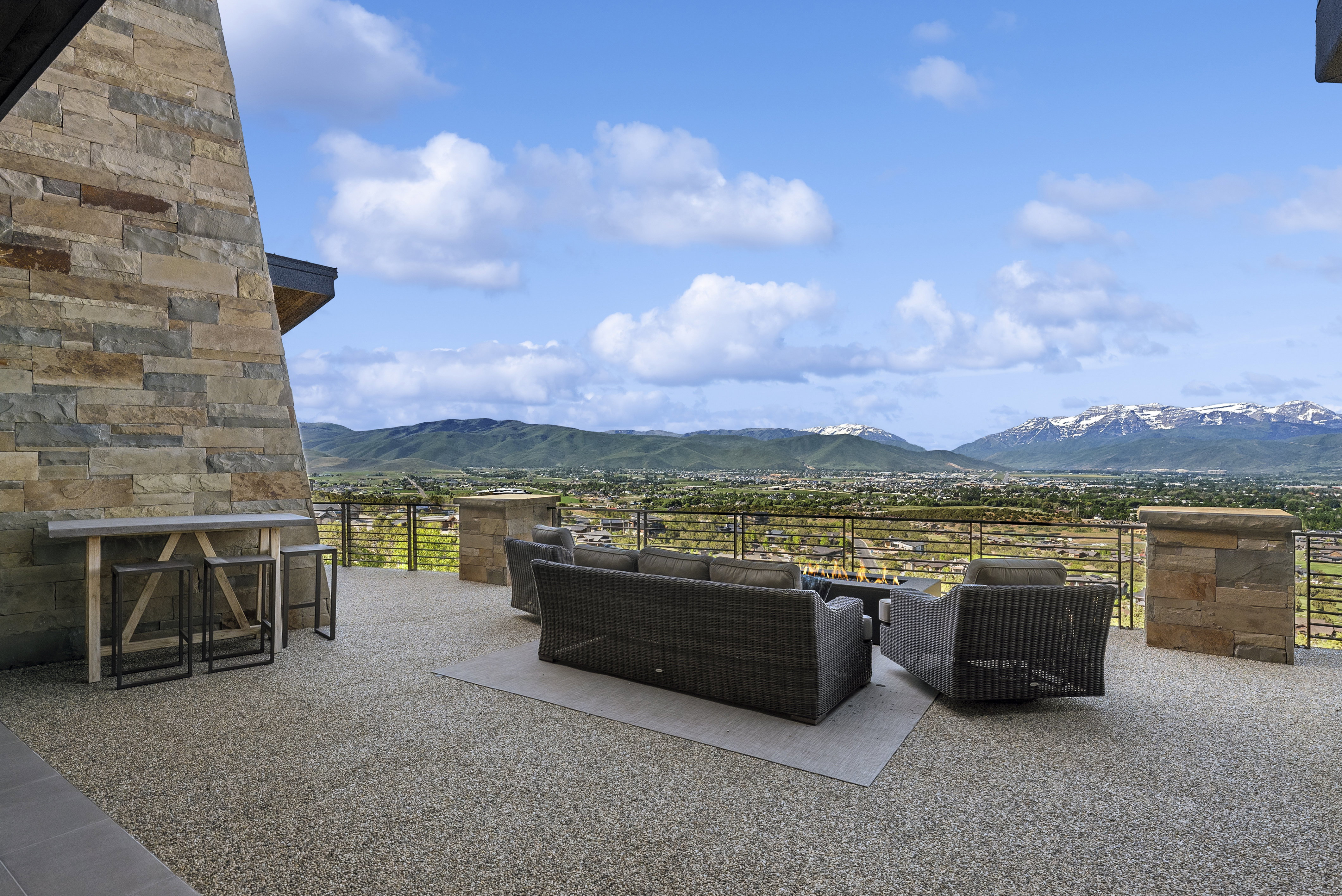 Expansive outdoor patio featuring a textured aggregate surface, a stone-clad exterior wall, and a low metal railing