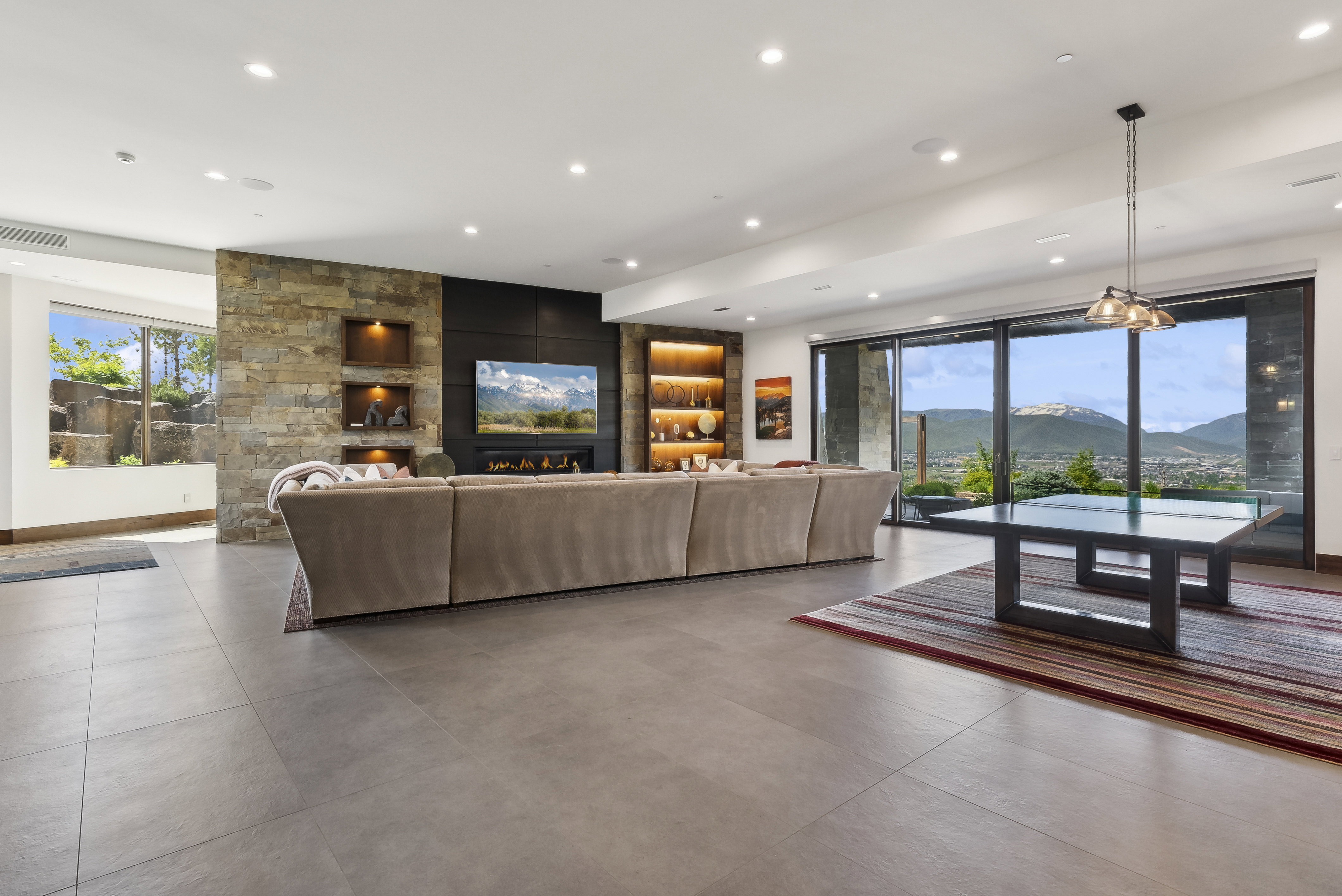Spacious living area featuring large format tile flooring, a stone accent wall with built-in display niches, and a linear fireplace below a mounted television