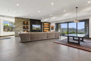 Spacious living area featuring large format tile flooring, a stone accent wall with built-in display niches, and a linear fireplace below a mounted television