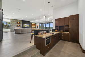 Contemporary wet bar featuring wood-finish cabinetry, stone countertops, an undermount sink, and a built-in microwave