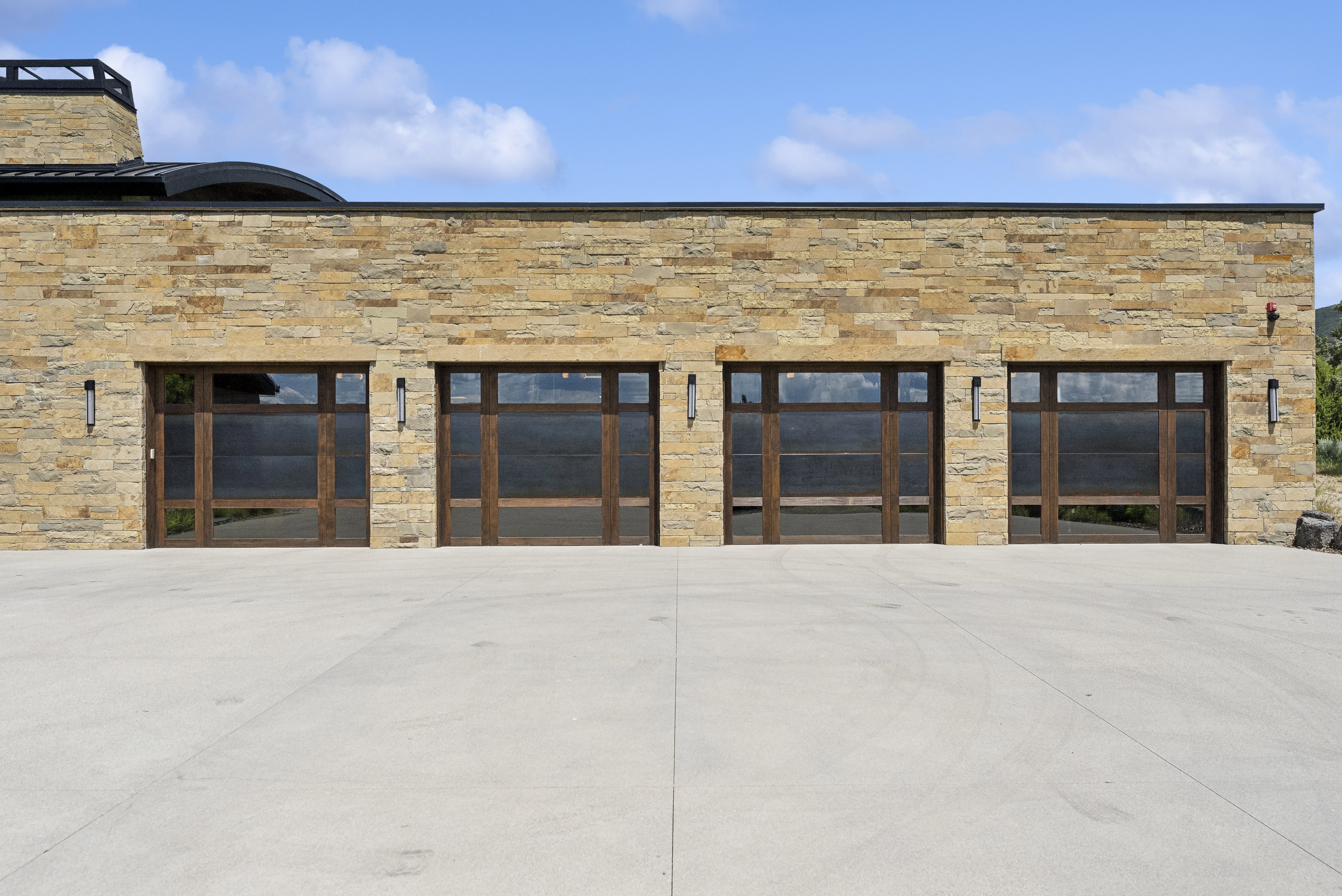 Stone facade with four contemporary garage doors featuring dark wood frames and frosted glass panels