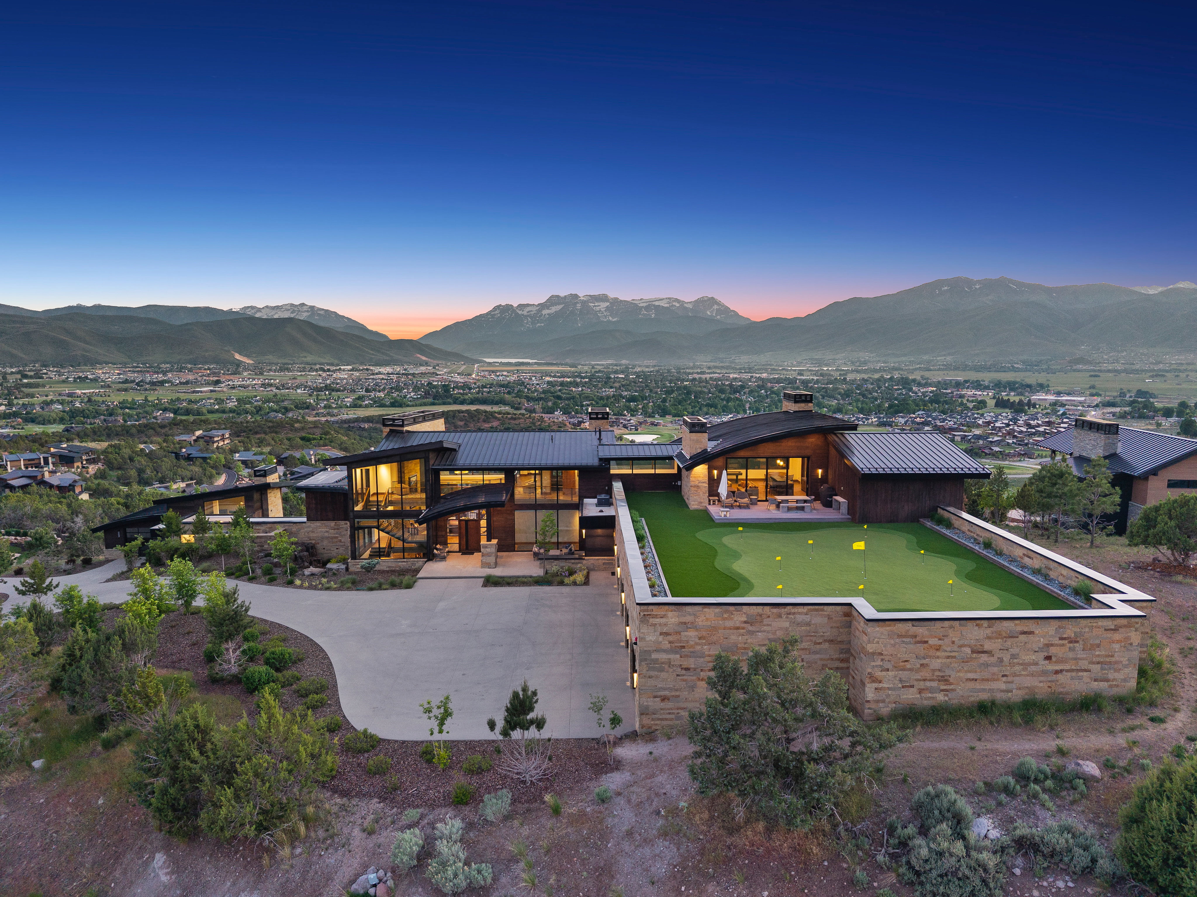 Contemporary residence featuring extensive glass facades, a multi-level putting green, and a curved driveway