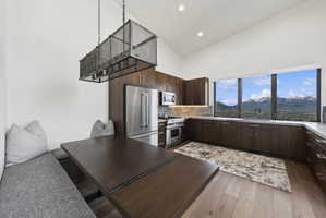 Modern kitchen featuring a built-in banquette, wood-finish flooring, dark wood cabinetry, stainless steel appliances, and a wall of expansive windows with a mountain backdrop