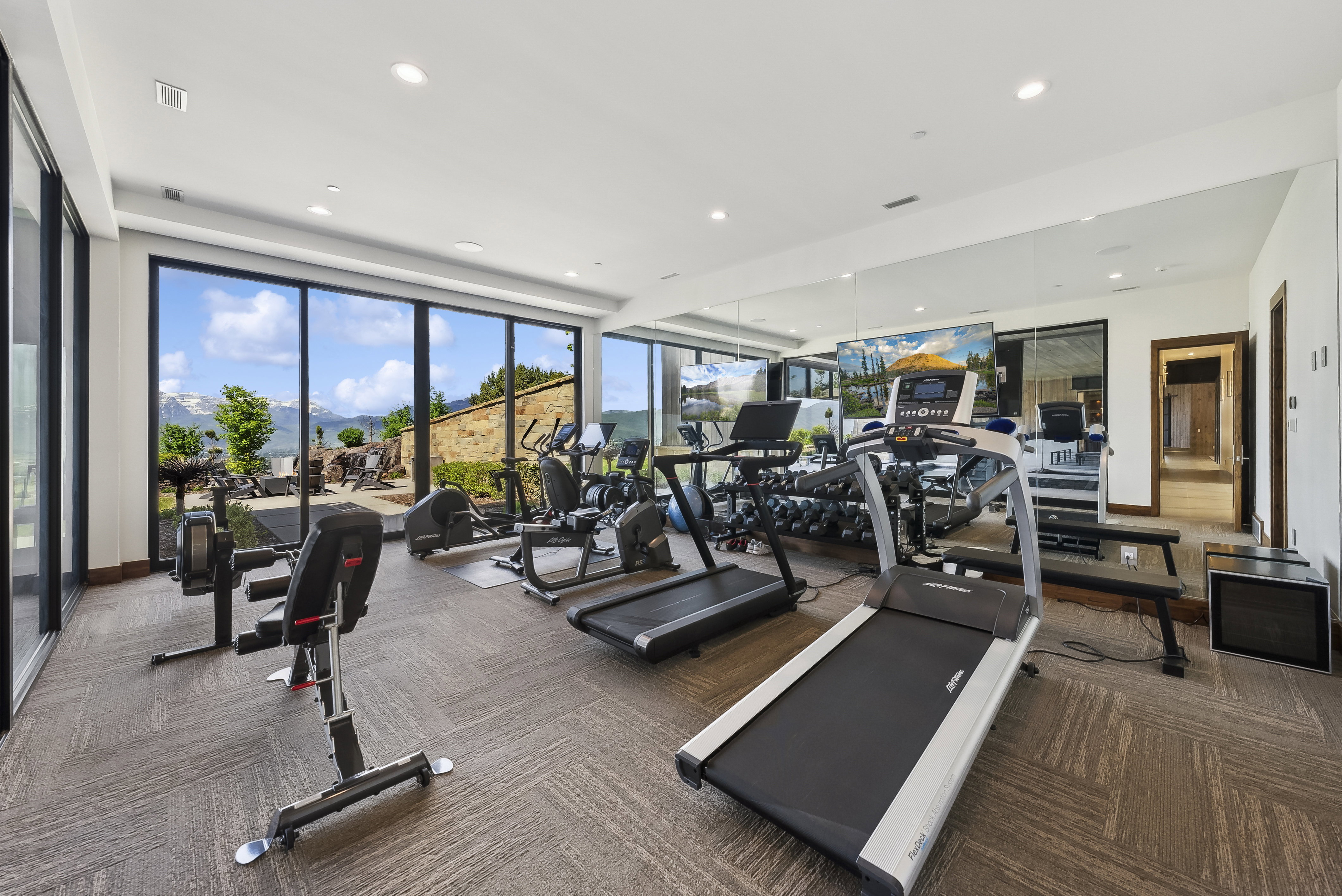 Dedicated fitness room featuring wall-to-wall mirrors, recessed lighting, and large format windows