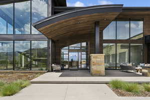 Contemporary architectural design featuring extensive window walls, wood-paneled exterior accents, a curved portico, and a stone-clad column