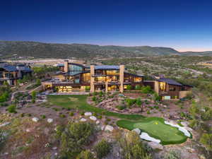 Contemporary multi-level residence featuring extensive glass facades, multiple outdoor terraces, integrated putting green, stone accents, and a sloped roofline