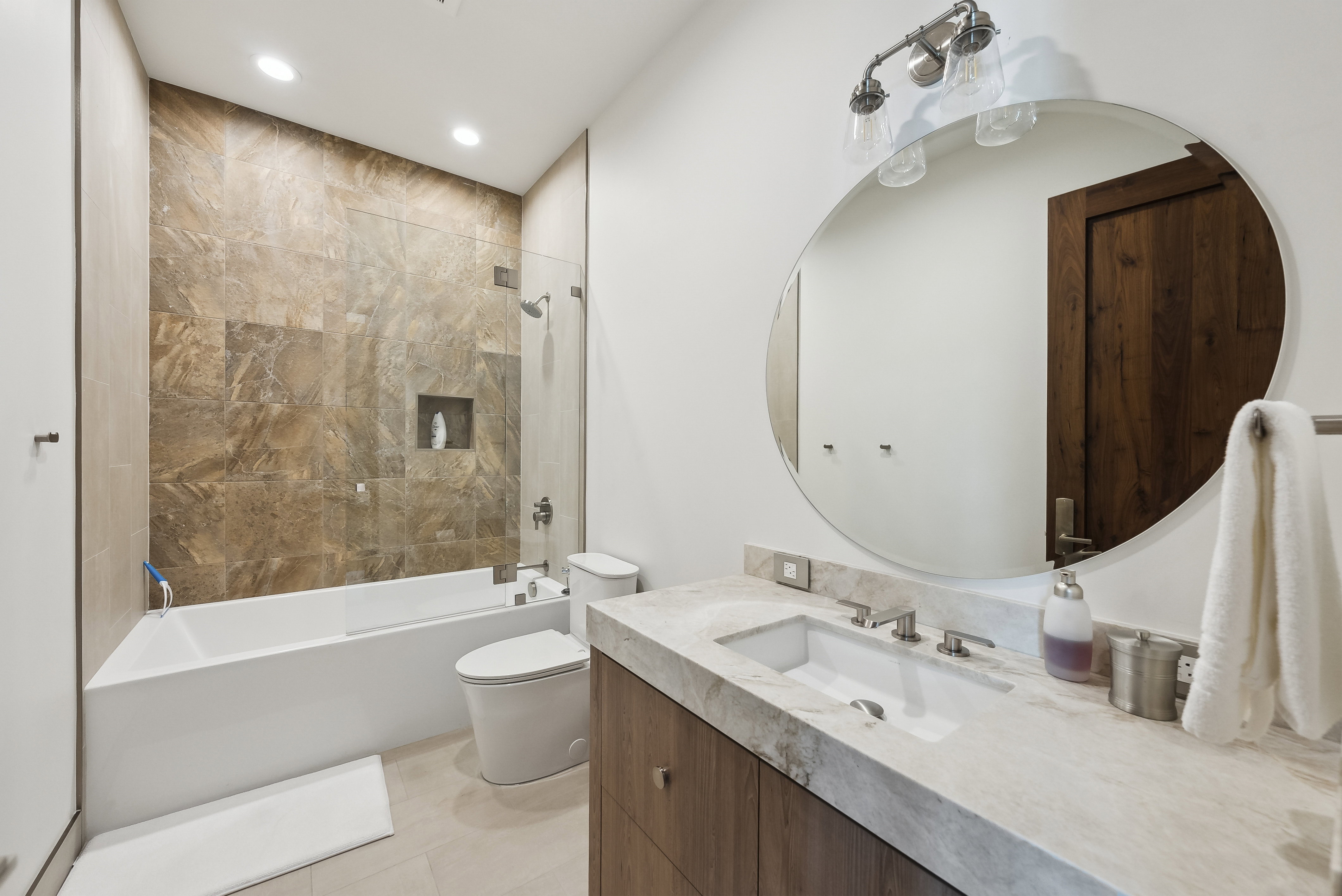 Contemporary bathroom featuring a built-in tub with a glass shower panel, an integrated shower niche, and extensive wall tiling