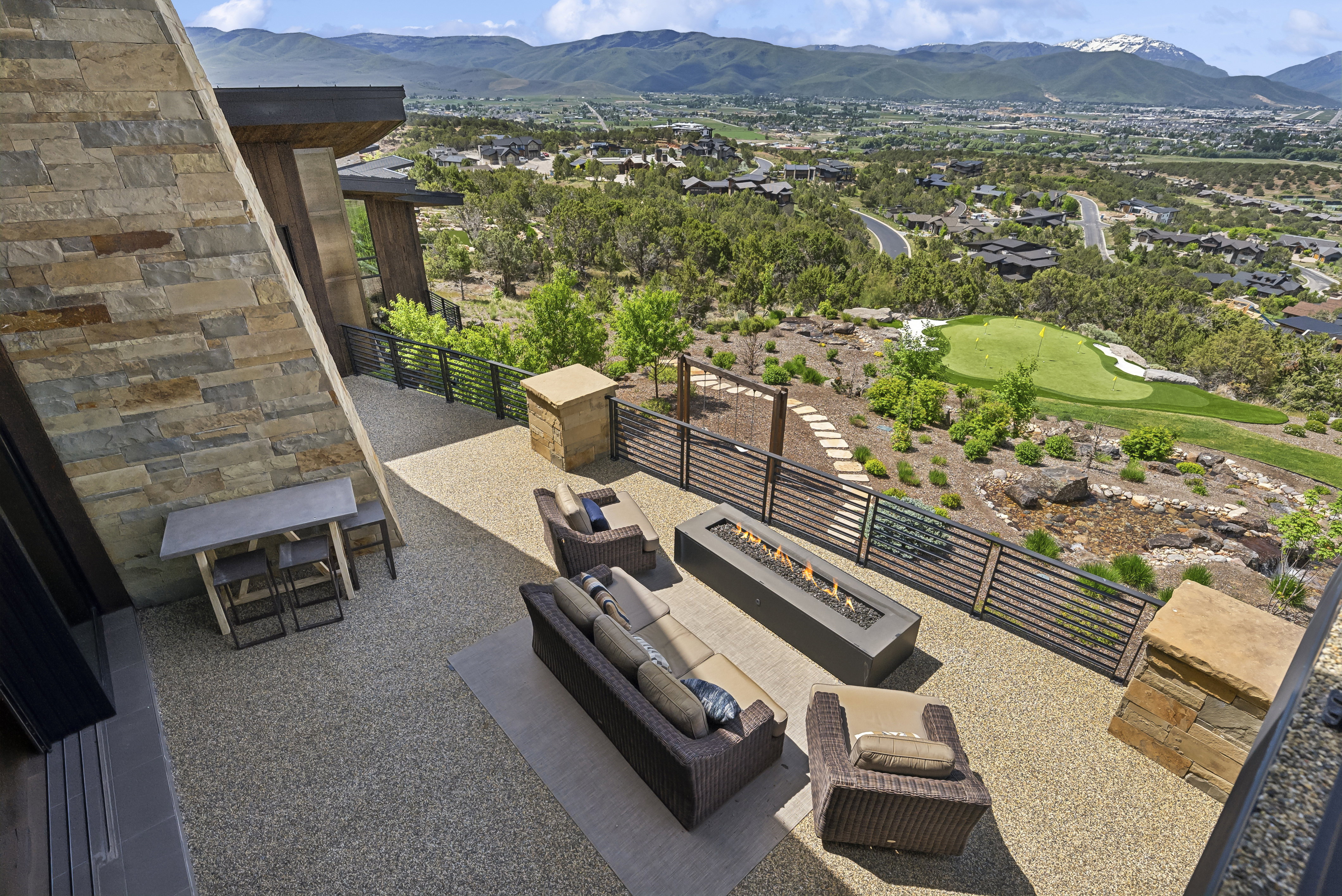 Expansive stone patio featuring a built-in fire pit, stone accent walls, and a visible golf green