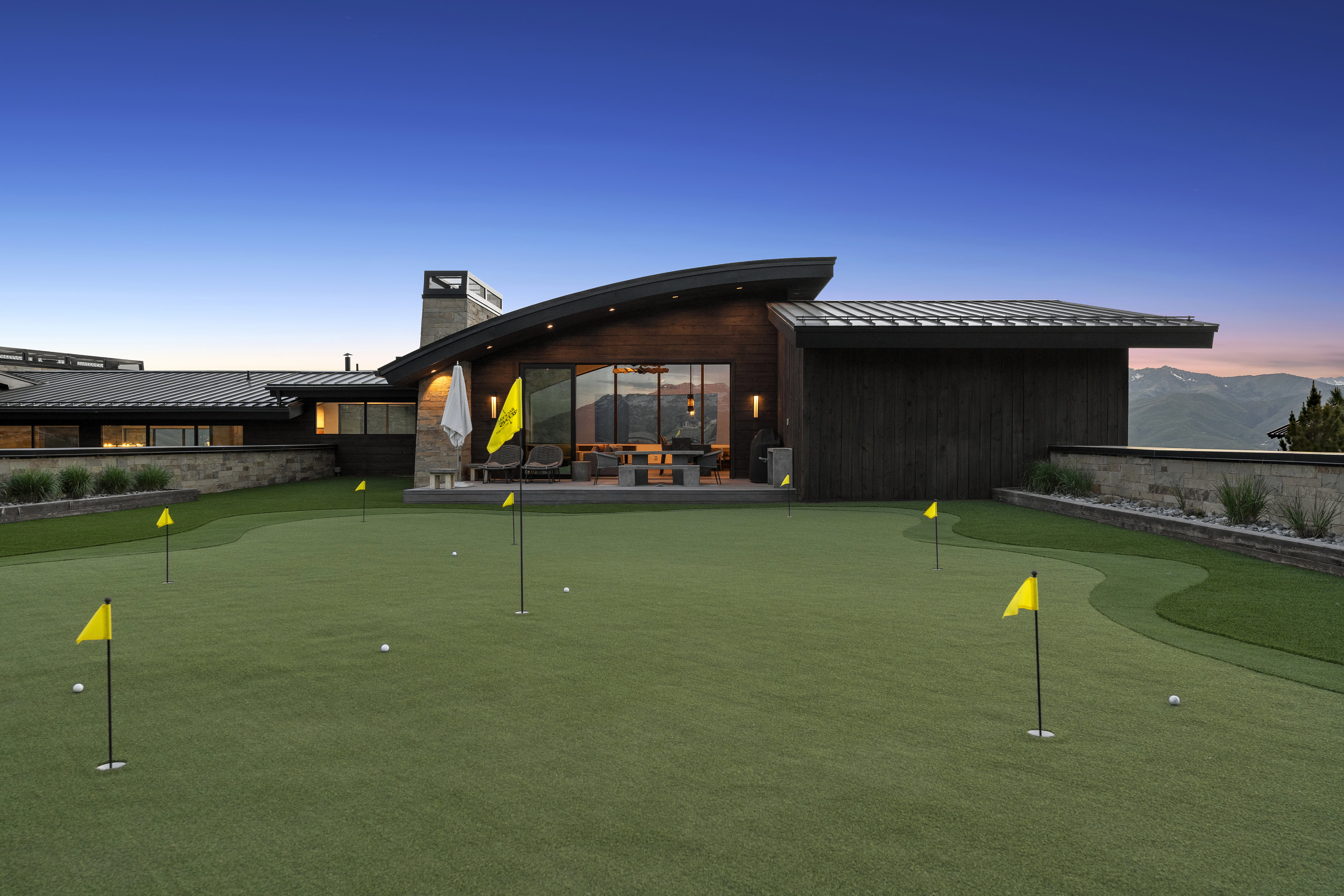 Putting green with multiple holes, accompanied by a stone retaining wall and distant mountain scenery