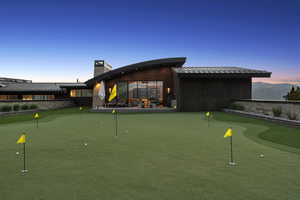 Putting green with multiple holes, accompanied by a stone retaining wall and distant mountain scenery