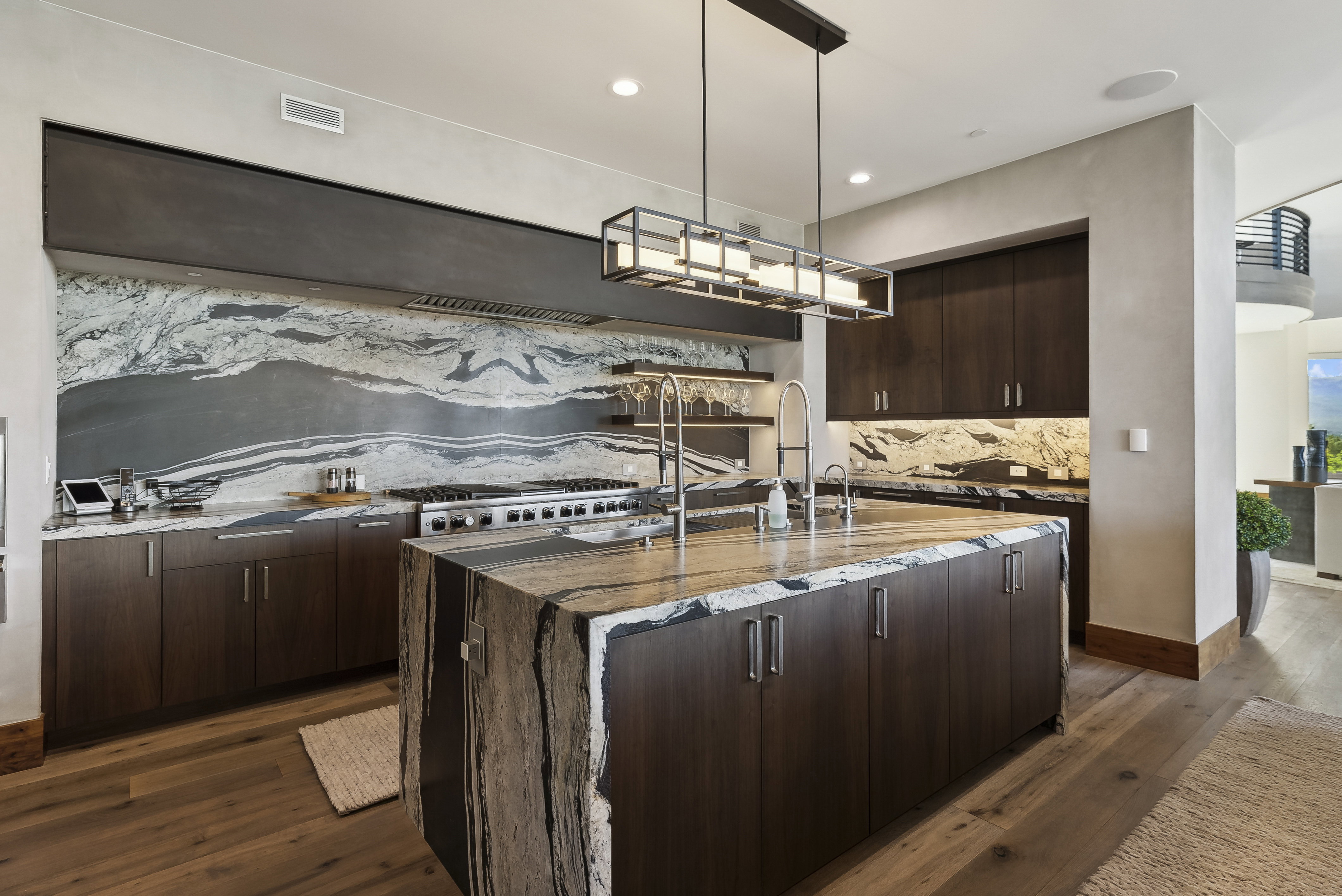 Gourmet kitchen featuring a substantial island with waterfall edge, integrated sink, and an architectural linear pendant light fixture