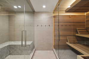 Spacious shower enclosure with a stone bench and an adjacent sauna featuring wood-paneled walls and tiered seating