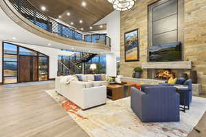 Grand living space featuring a two-story stone fireplace with a substantial hearth, wood-finish flooring, and a curved second-story balcony with metal railings