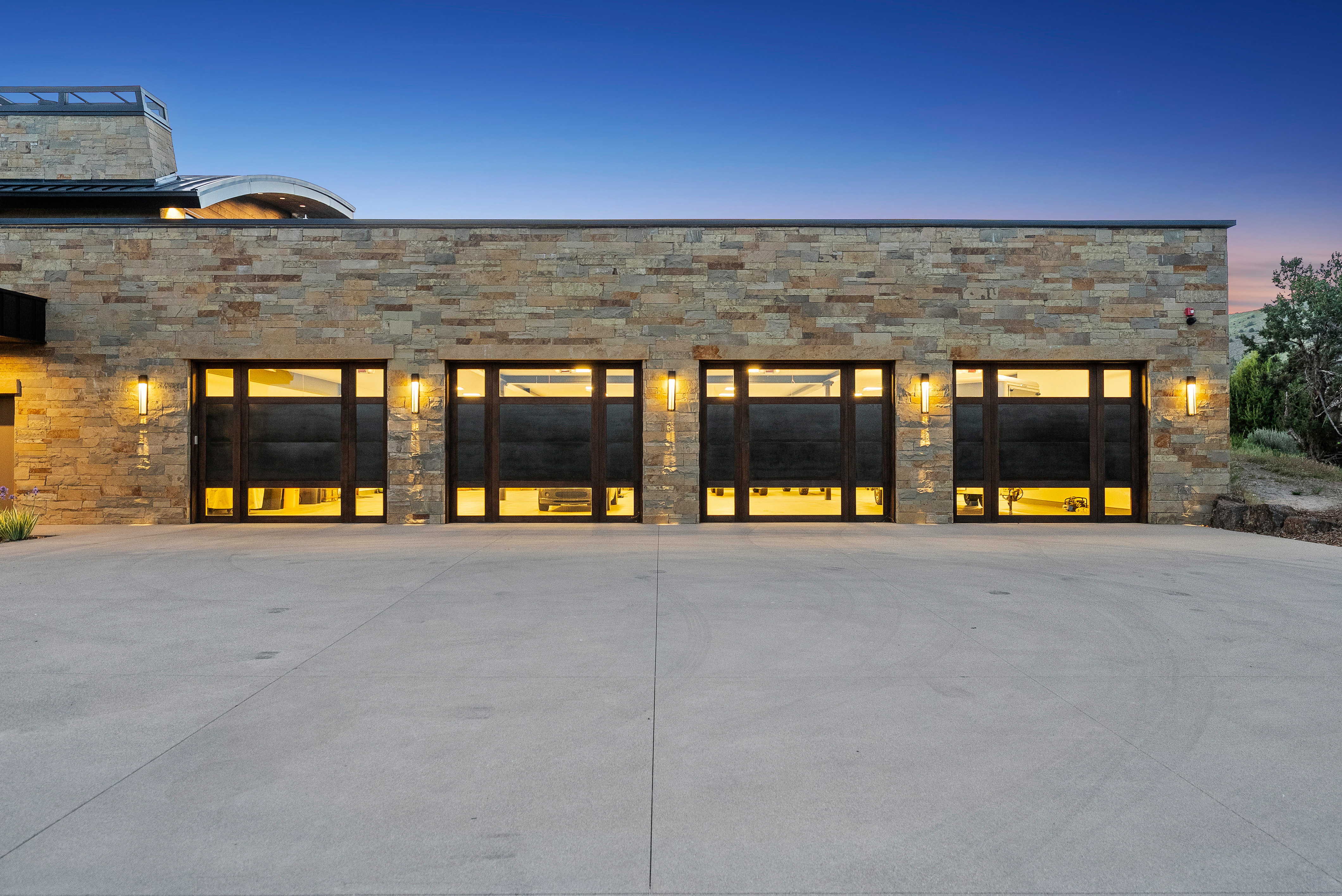 Stone facade property featuring four modern garage doors with frosted glass panels, exterior sconce lighting, and a concrete driveway