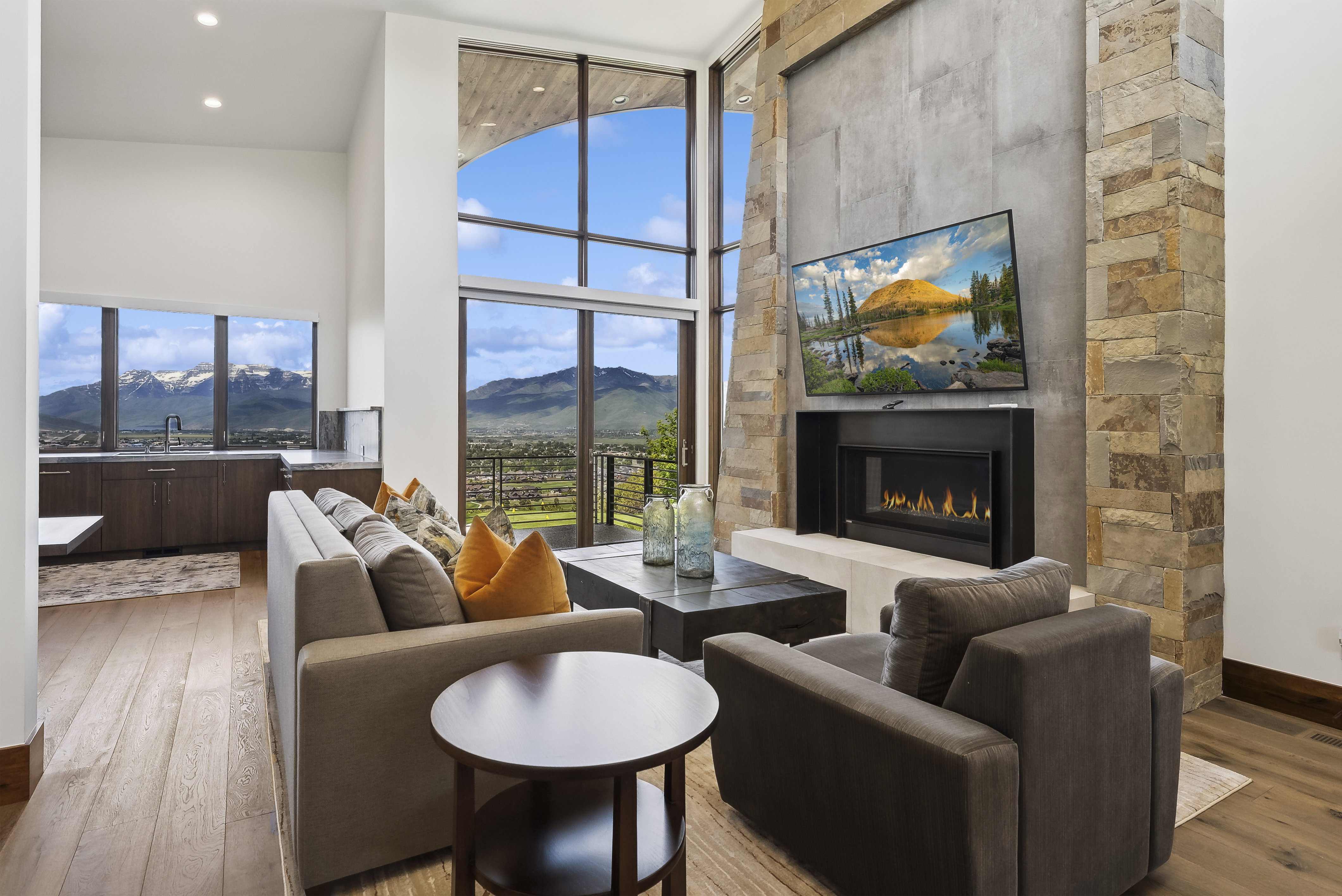 Spacious living area featuring expansive floor-to-ceiling windows, a stone-clad fireplace with a built-in fire feature, and light wood-finish flooring
