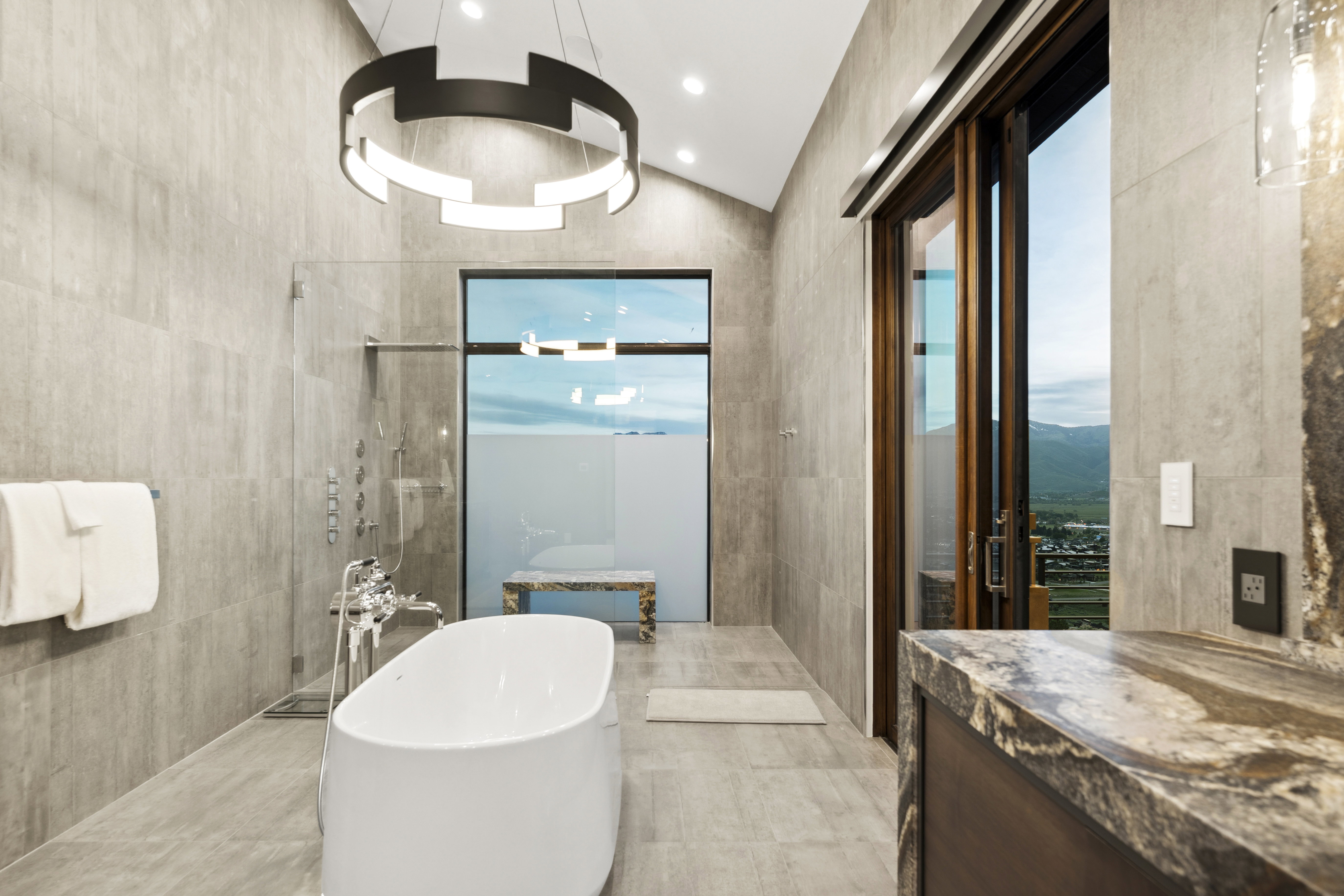 Contemporary bathroom featuring a freestanding soaking tub, glass-enclosed shower, and a dramatic vaulted ceiling with a modern chandelier