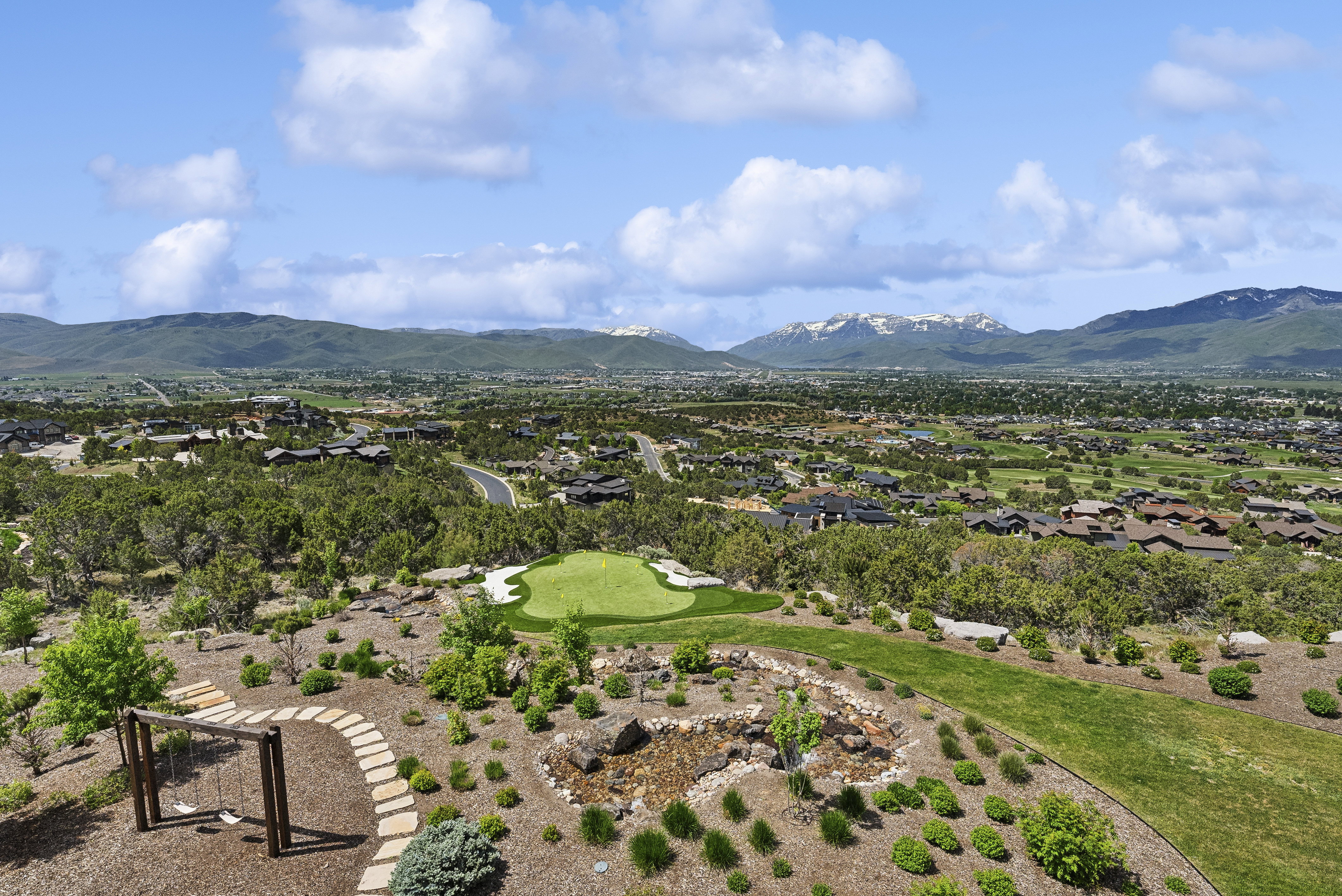 Expansive hillside property featuring a private putting green, a stone path, and a wooden swing set