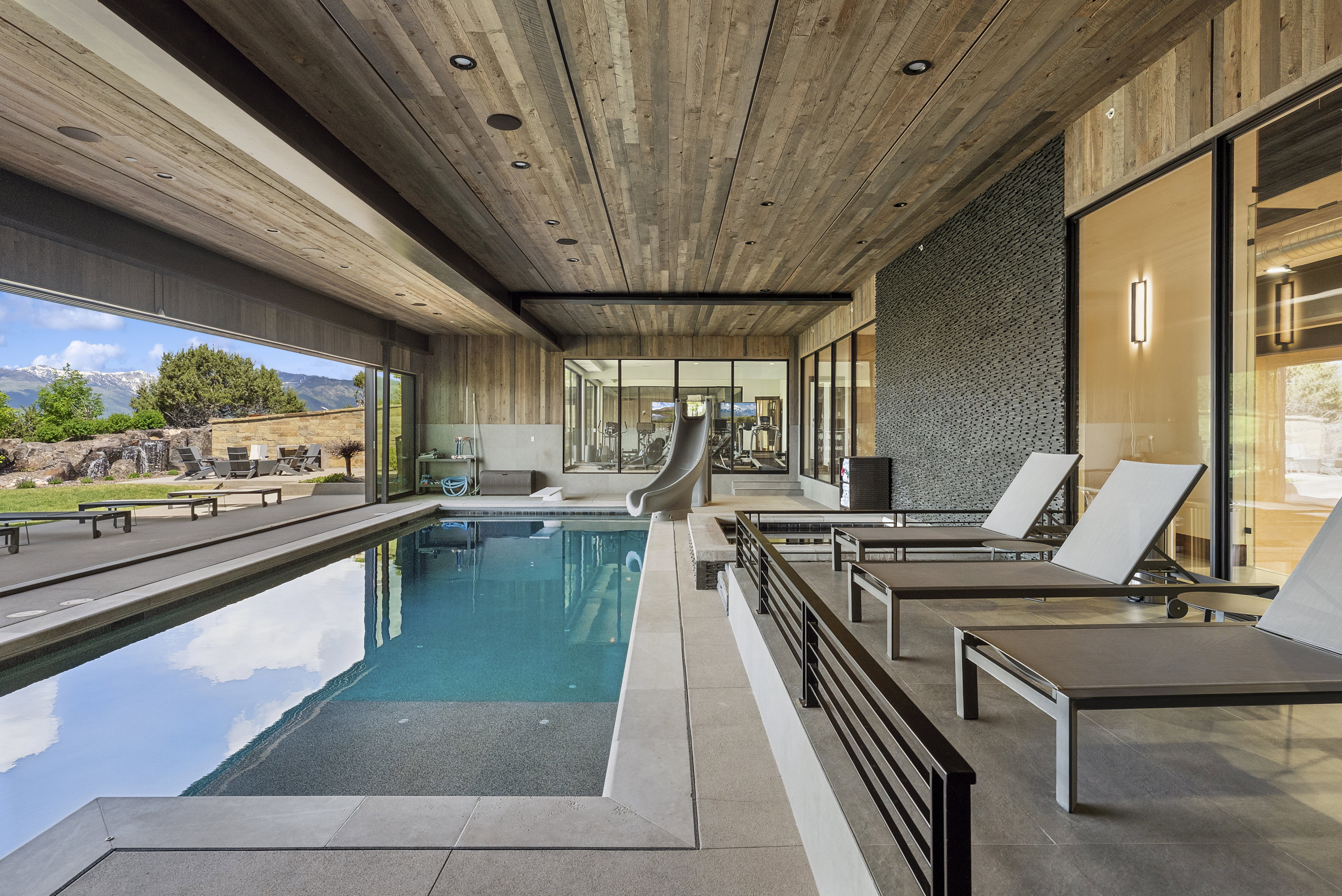 Indoor swimming pool featuring wood-finish ceiling, large format tile flooring, and a sliding glass wall