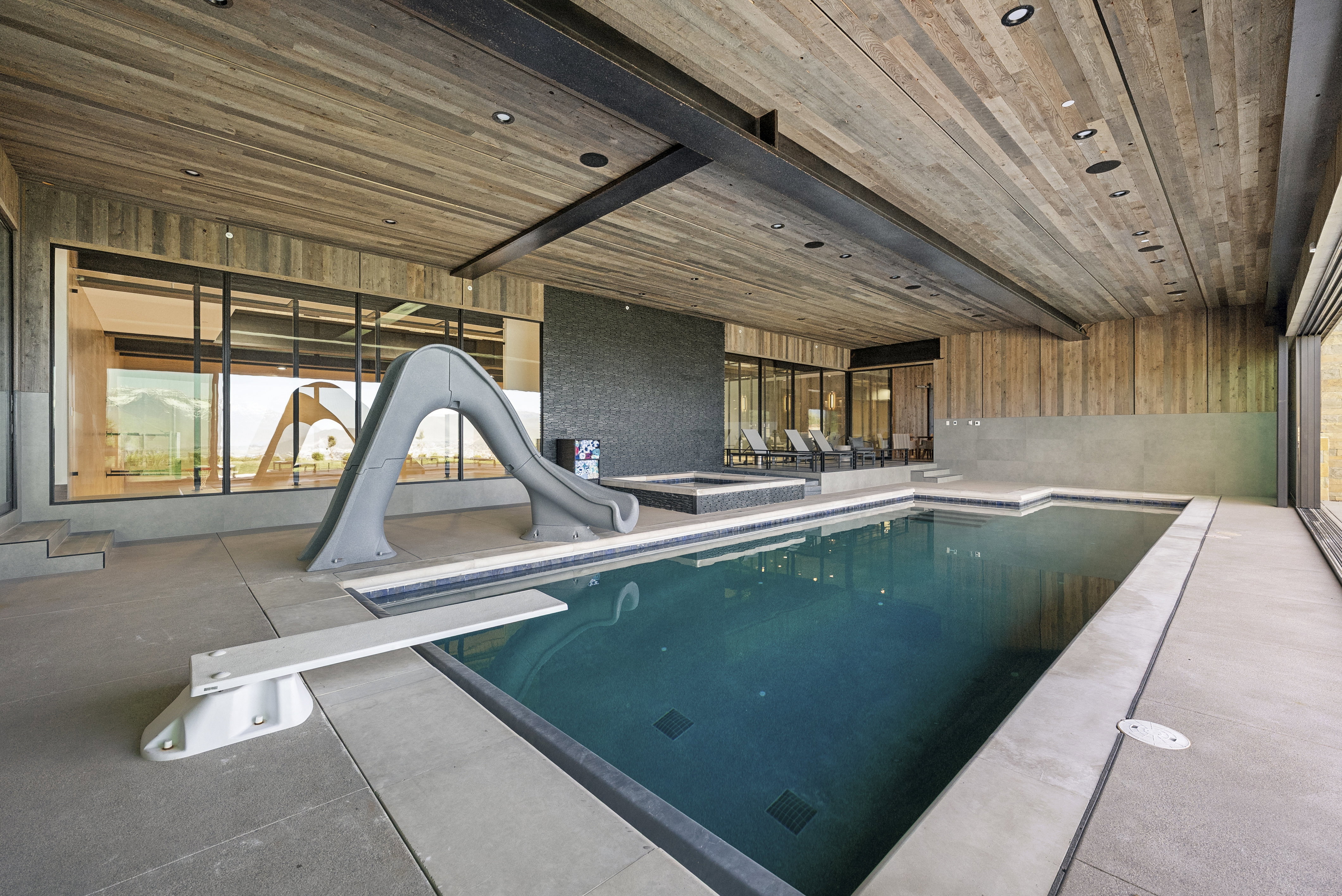 Indoor swimming pool with a diving board and attached slide, complemented by a raised hot tub area