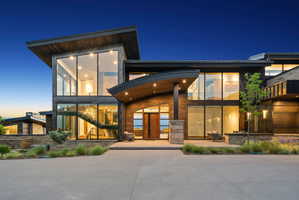 Contemporary architectural design featuring expansive glass panels, wood siding, stone accents, and a curved entryway canopy