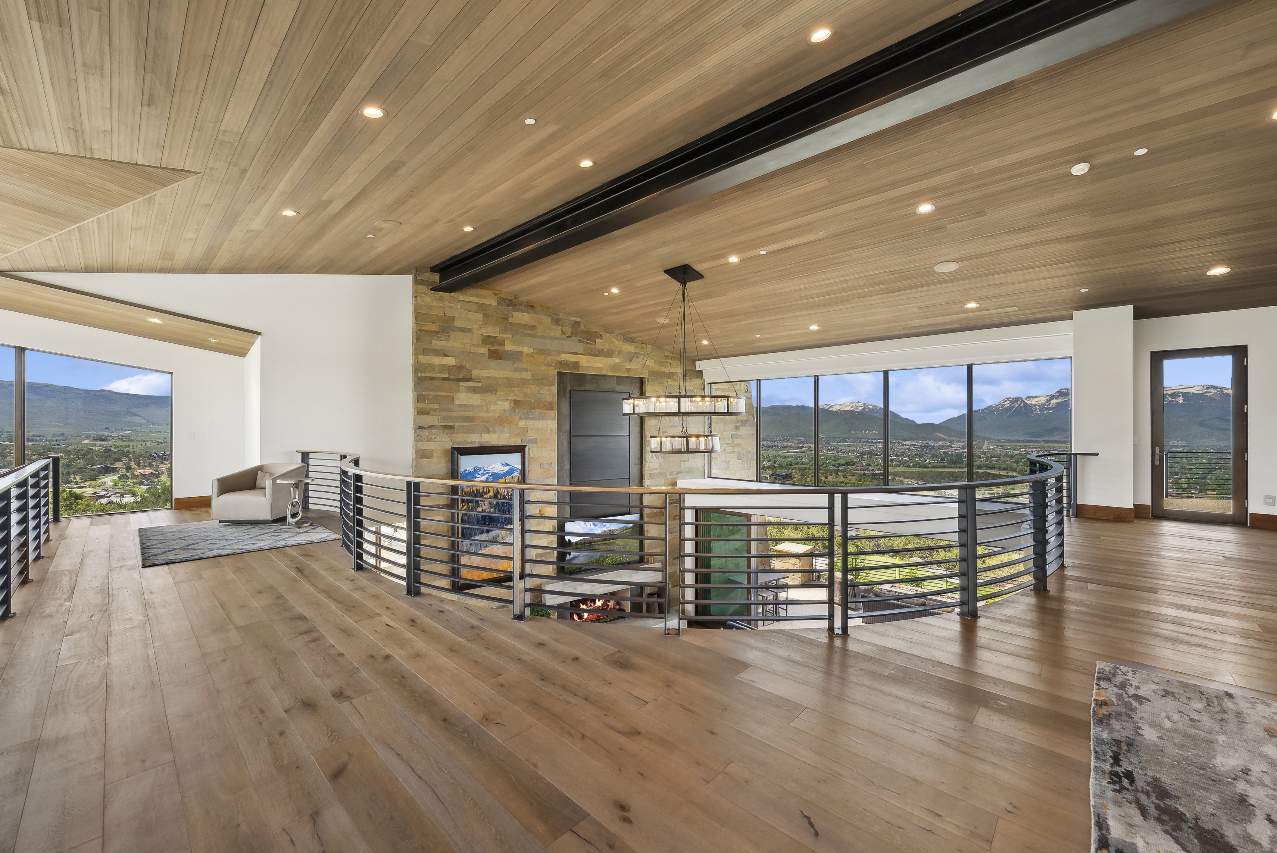 Open upper-level space featuring wood-finish flooring, a wood-paneled ceiling with recessed lighting, and a stone accent wall