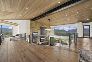Open upper-level space featuring wood-finish flooring, a wood-paneled ceiling with recessed lighting, and a stone accent wall