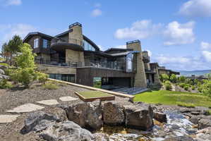 Multi-level modern home featuring stone and wood-finish siding, extensive glass, multiple balconies, and a putting green